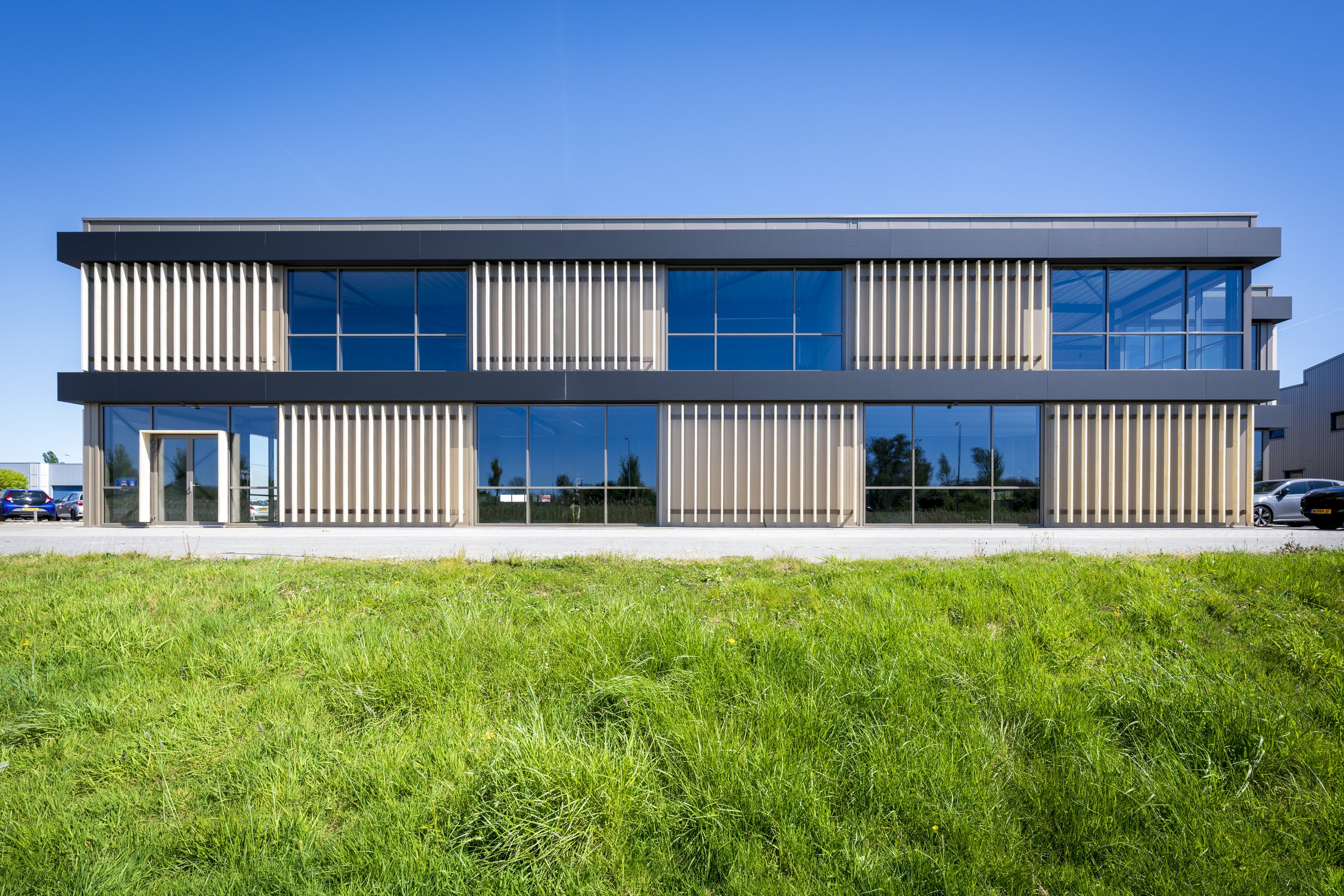 Modern kantoorgebouw met grote ramen en verticale houtpanelen onder een blauwe hemel.