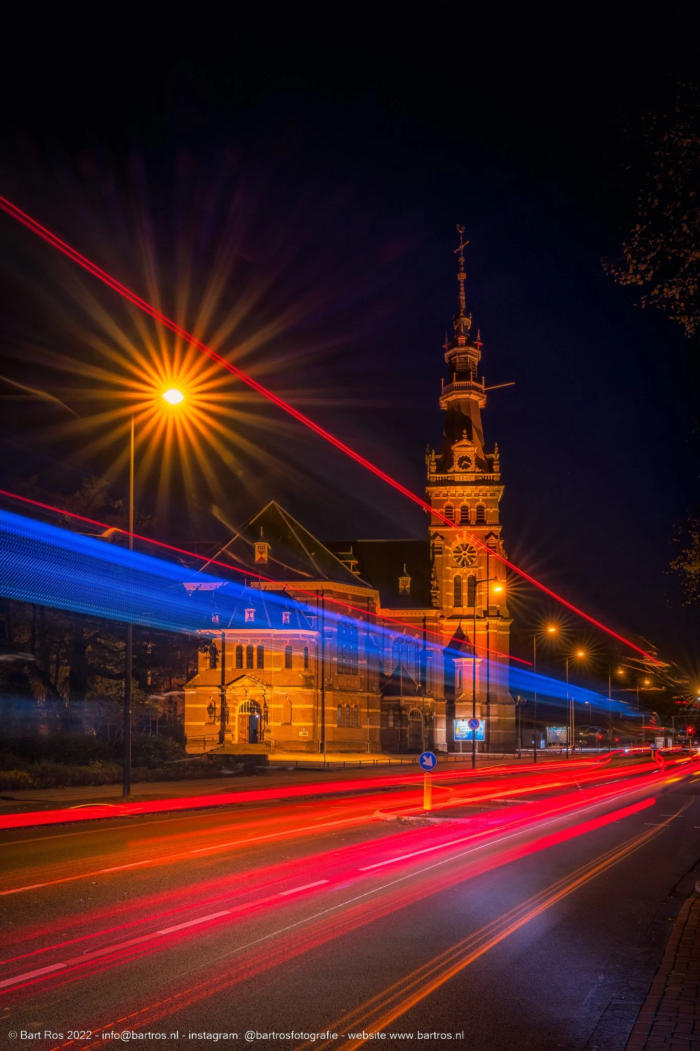 Een lang exposure foto van een kerktoren bij nacht met lichtstrepen van passerende auto's.