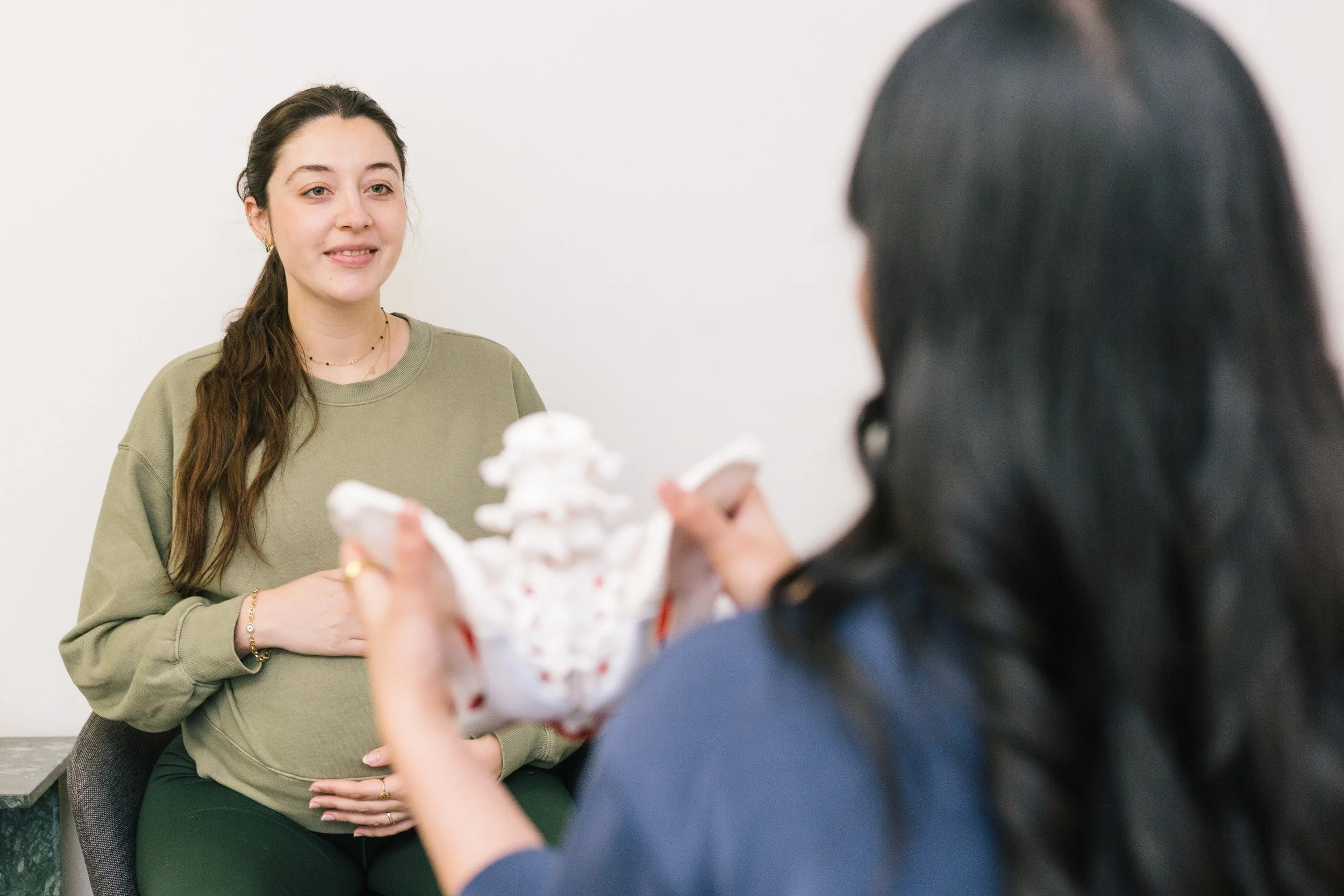 Physical therapist uses a pelvic model to explain anatomy and treatment options to a pregnant patient during a prenatal consultation