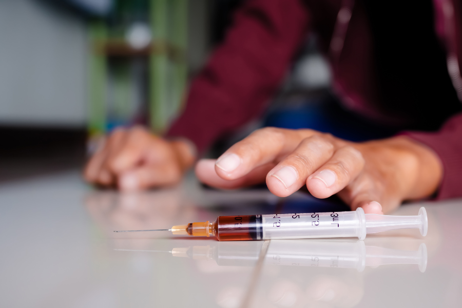 A person preparing to administer an injection with a filled syringe on a white surface.