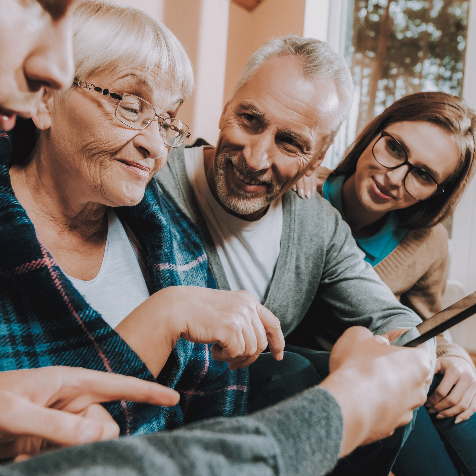 Four people, including elderly woman, middle-aged man, and two women, gathered around looking at a phone together, smiling and enjoying each other's company.