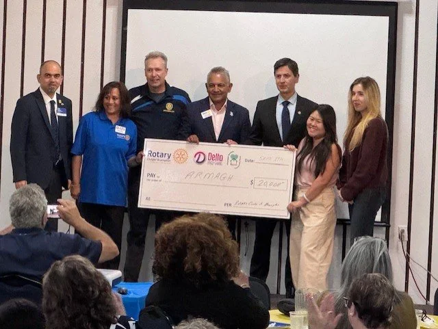 Group of people on stage presenting a large check to a recipient at an event with an audience seated in front.
