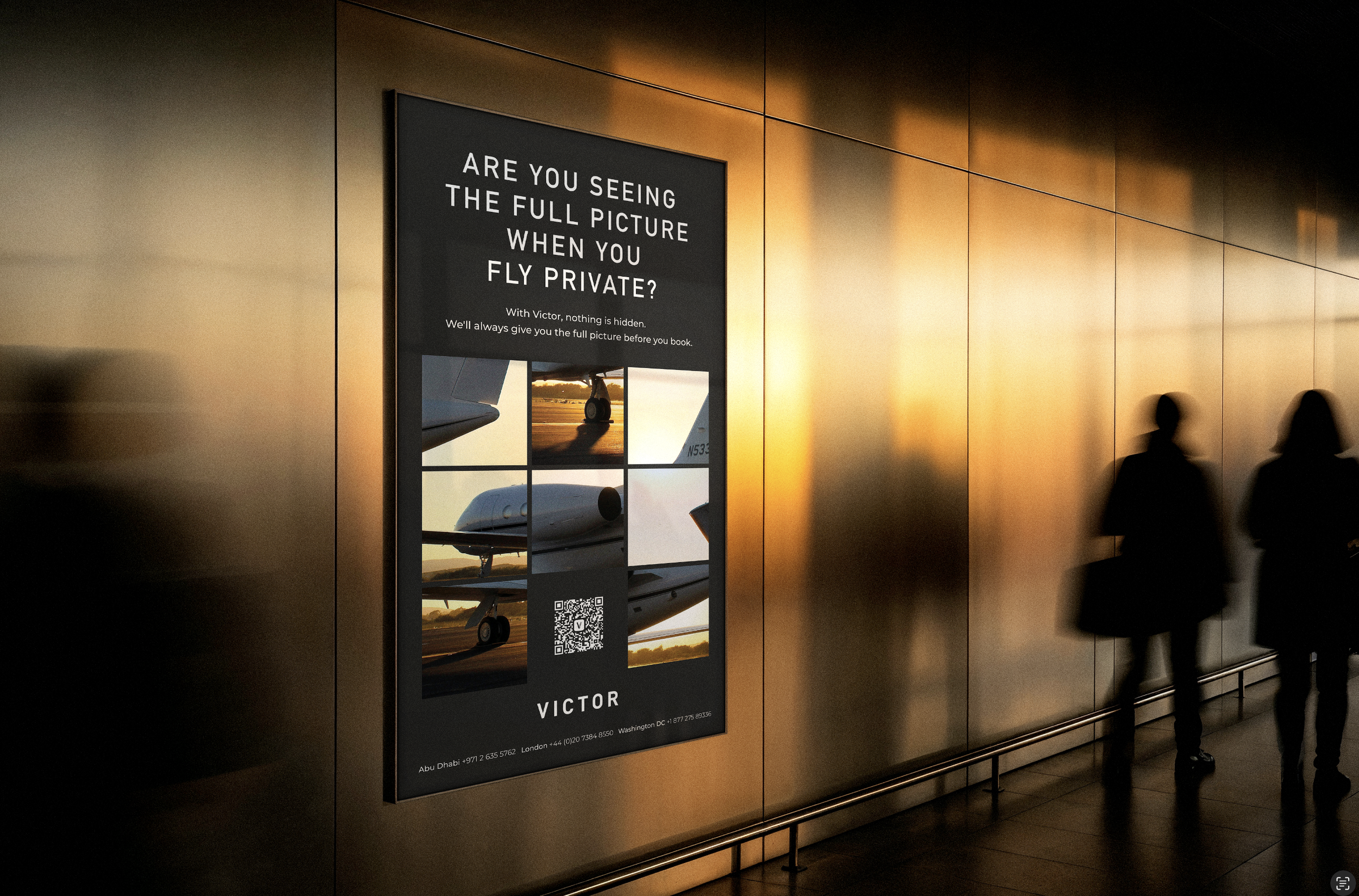 An airport digital display advertising a flight with the slogan, 'Are you seeing the full picture when you fly private?' with images of private jets and contact details for different locations, set against a check-in area wall with two silhouetted travelers passing by.
