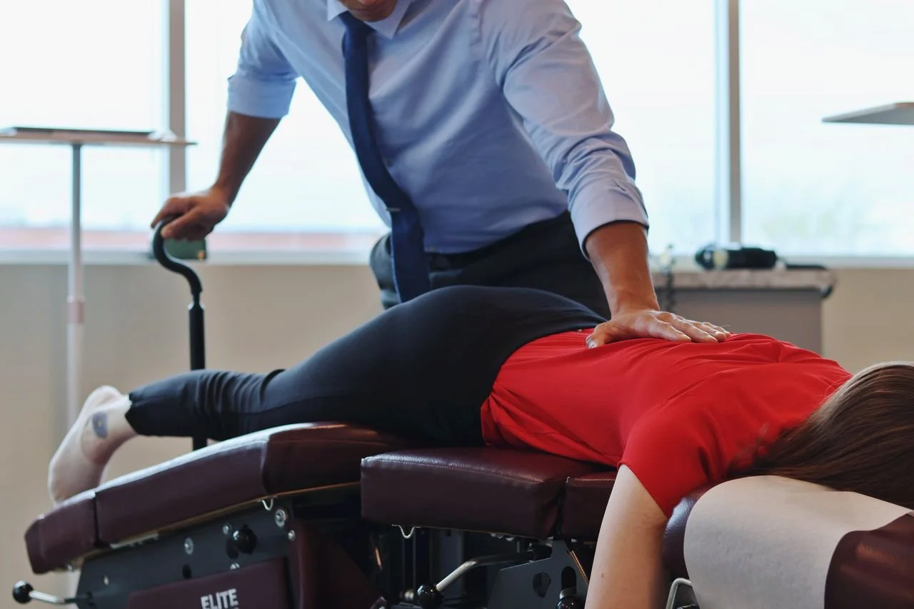 A chiropractor adjusting a woman lying face down on a treatment table in a clinic setting.