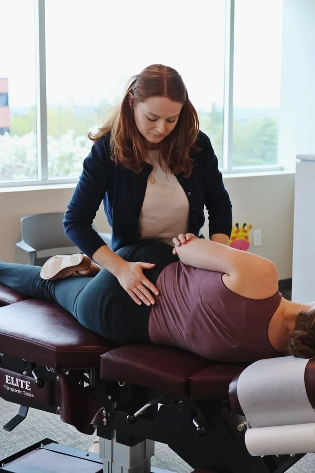 Chiropractor performing a back adjustment on a patient lying face down on a chiropractic table in an office with large windows in Colchester Vermont