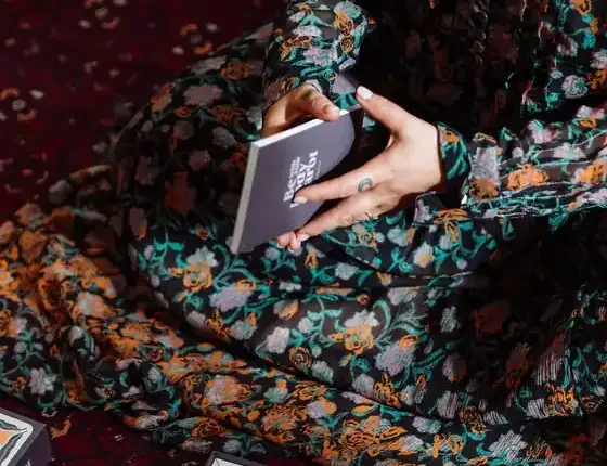 Hands holding the Be With Your Body Tarot guidebook with tarot cards on a rug