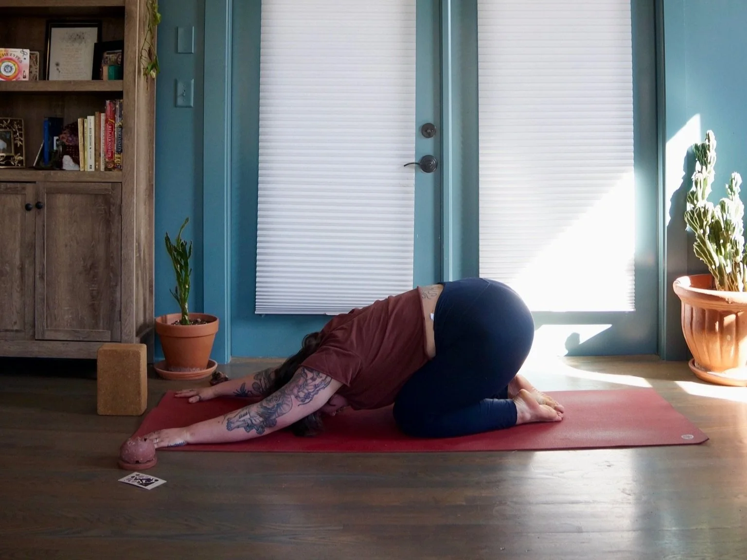 A person practicing yoga in a child's pose on a red mat in a sunlit room.