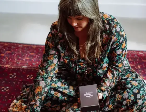 Sarah Jane Chapman holding the Be With Your Body Tarot deck on a red rug