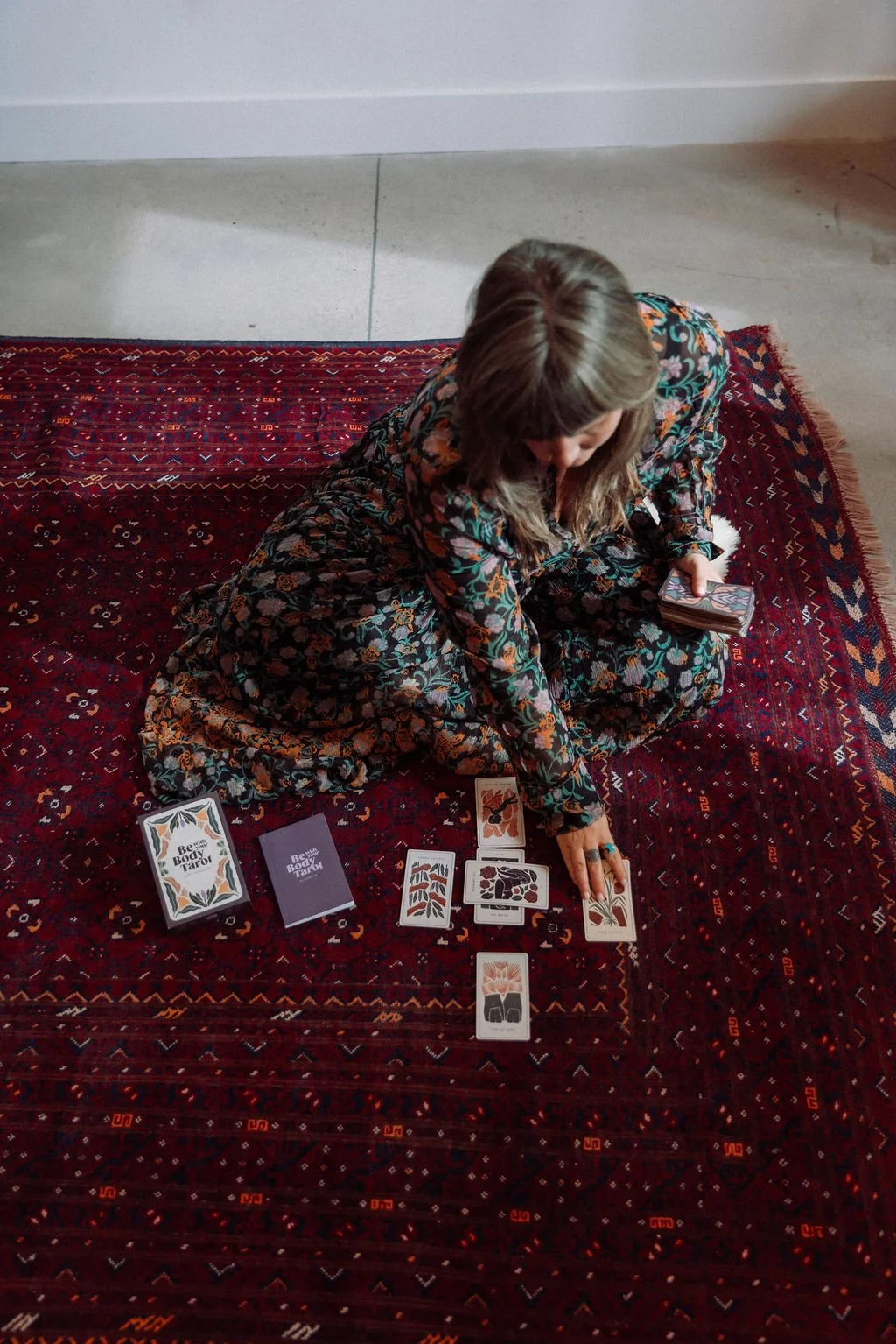 Sarah Jane shuffling tarot cards on a red rug beside a spread
