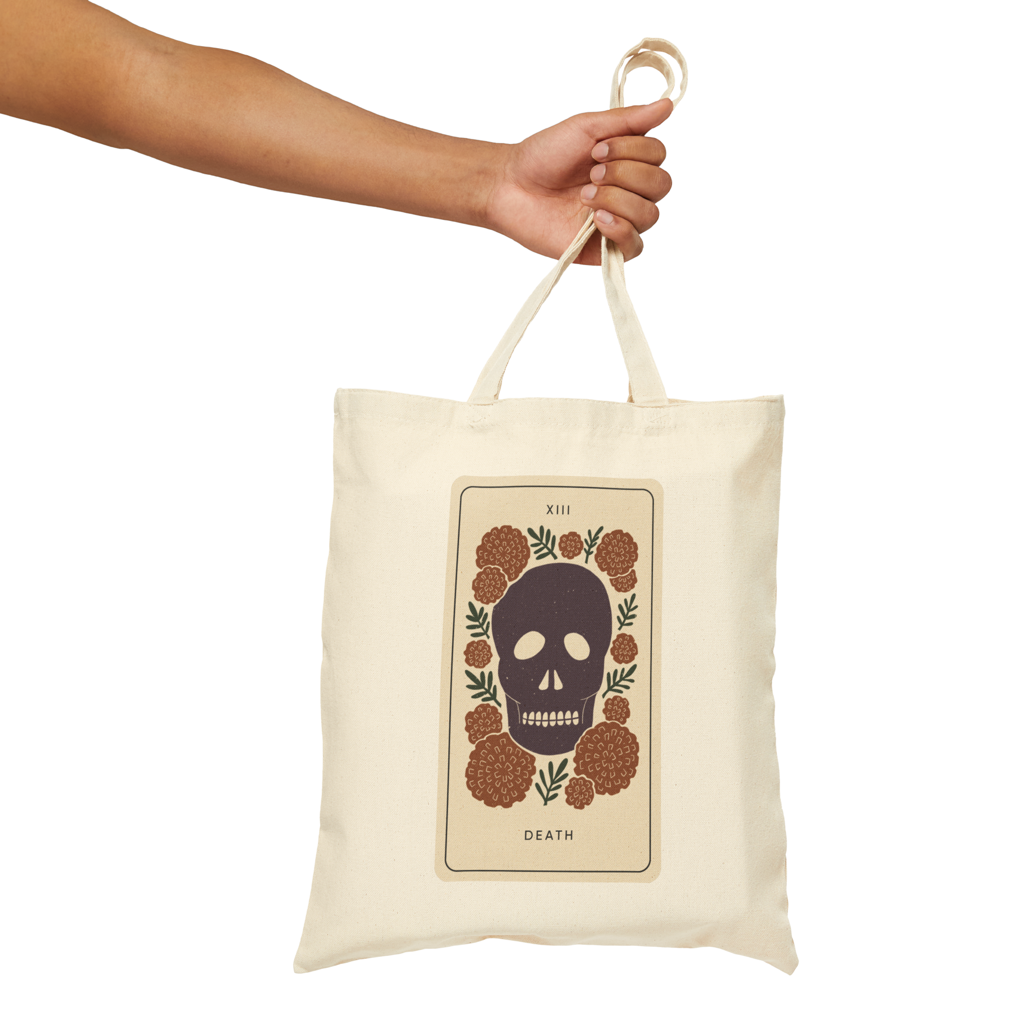 A person is holding a white reusable tote bag with a graphic of a skull surrounded by flowers and the word 'Death' underneath.