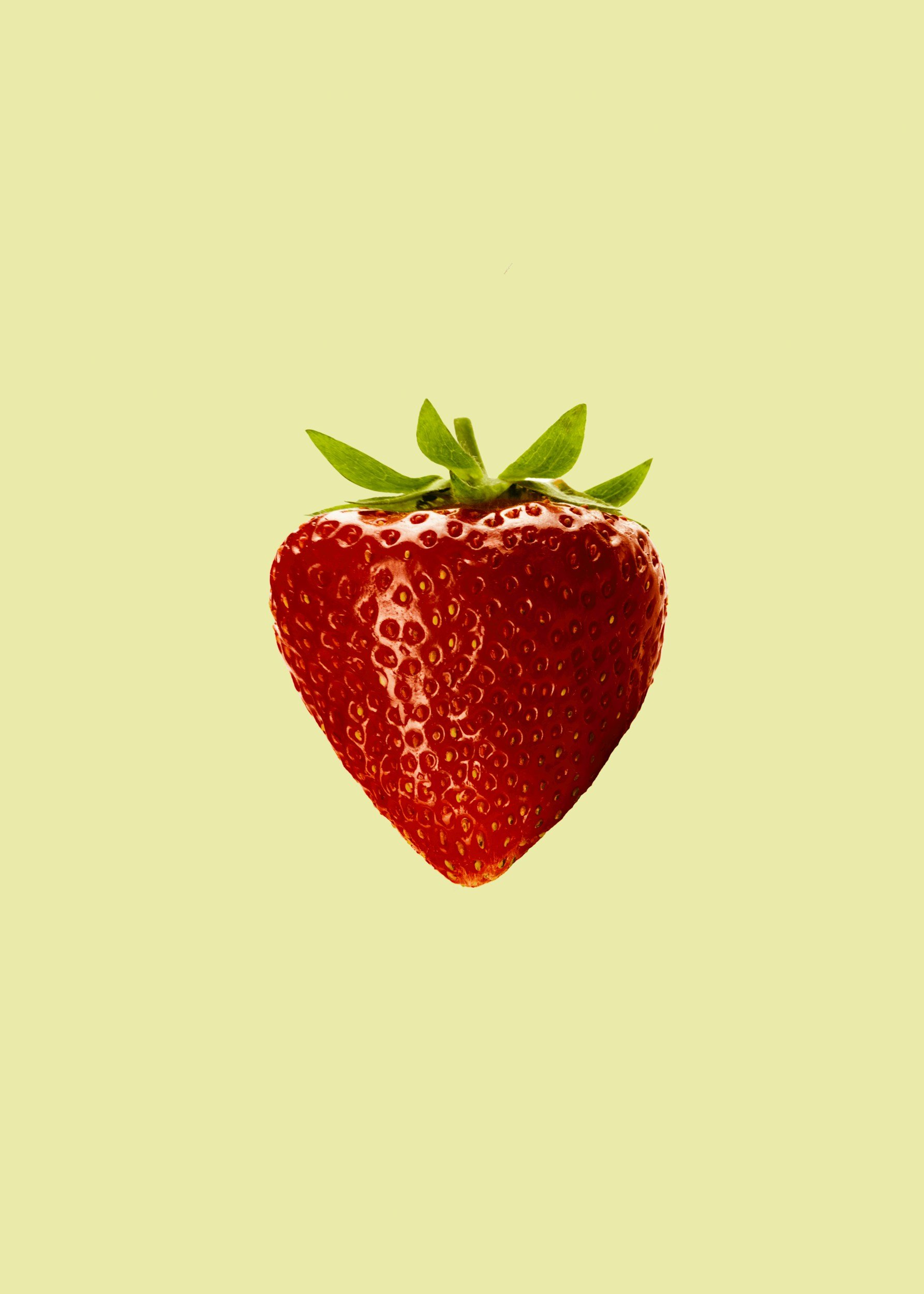 A close-up of a ripe red strawberry with green leaves on a light background.