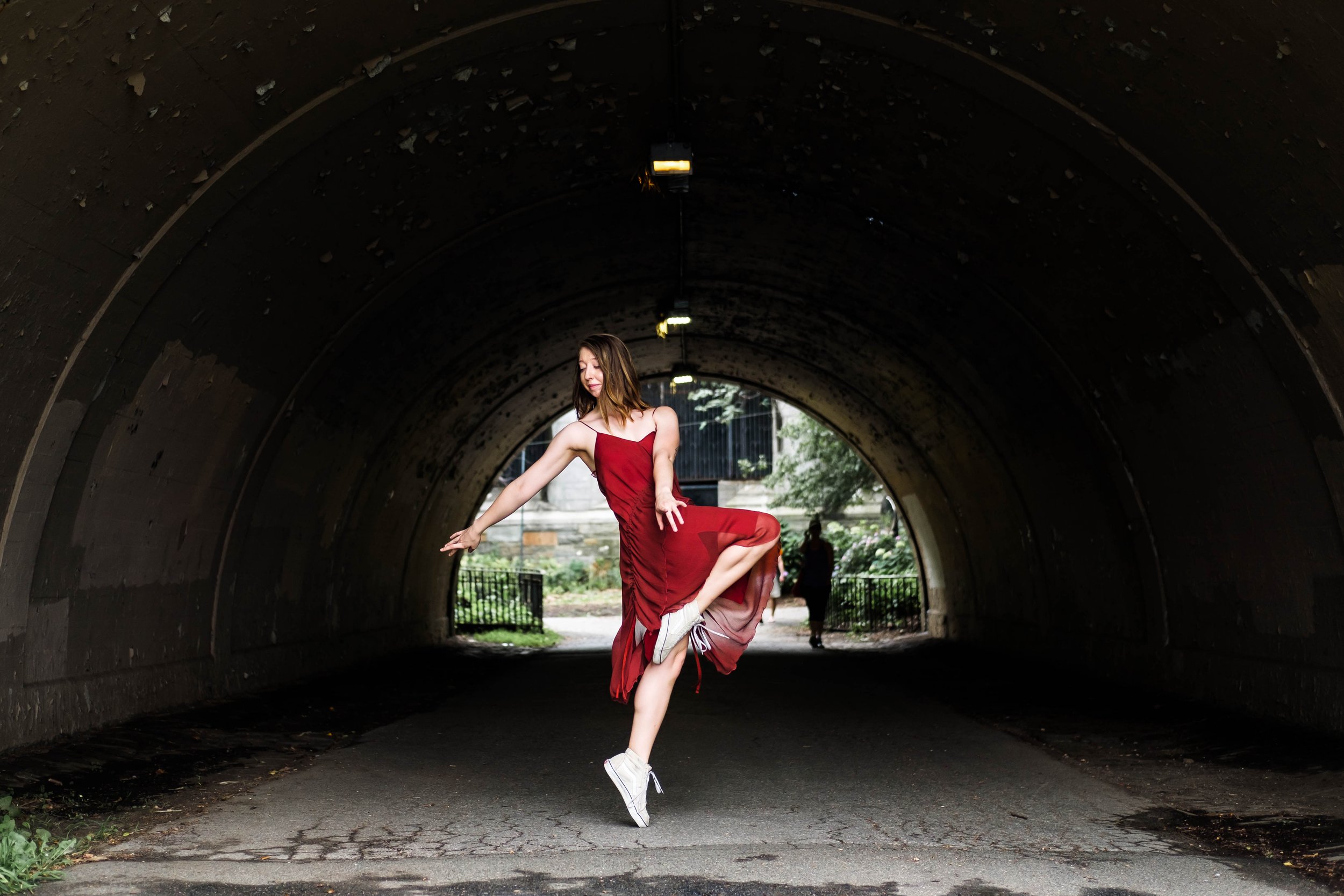 A woman in a red dress balancing on one foot in a tunnel.