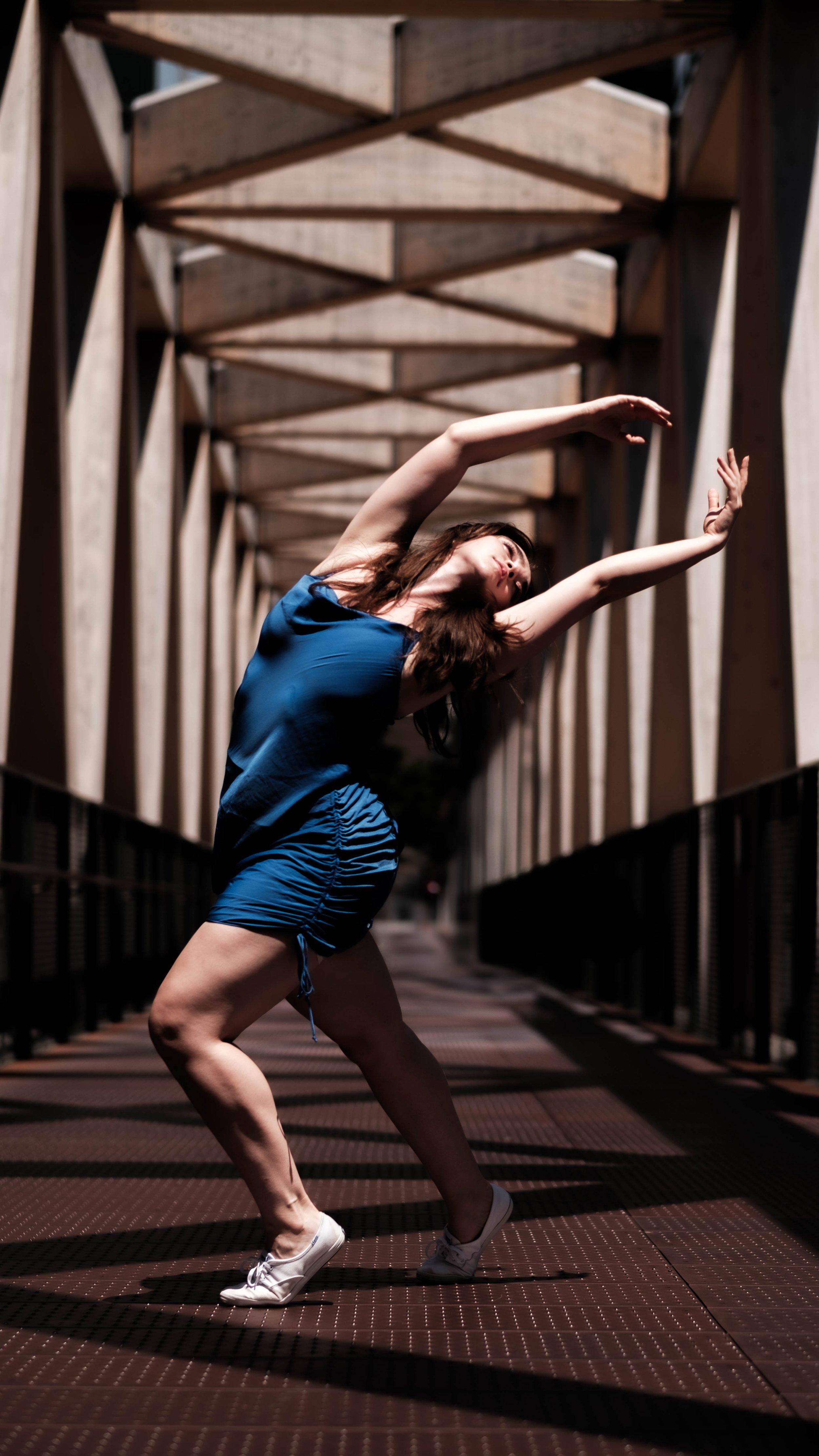 Woman in blue athletic outfit stretching on a metal bridge with wooden beams overhead during daytime.