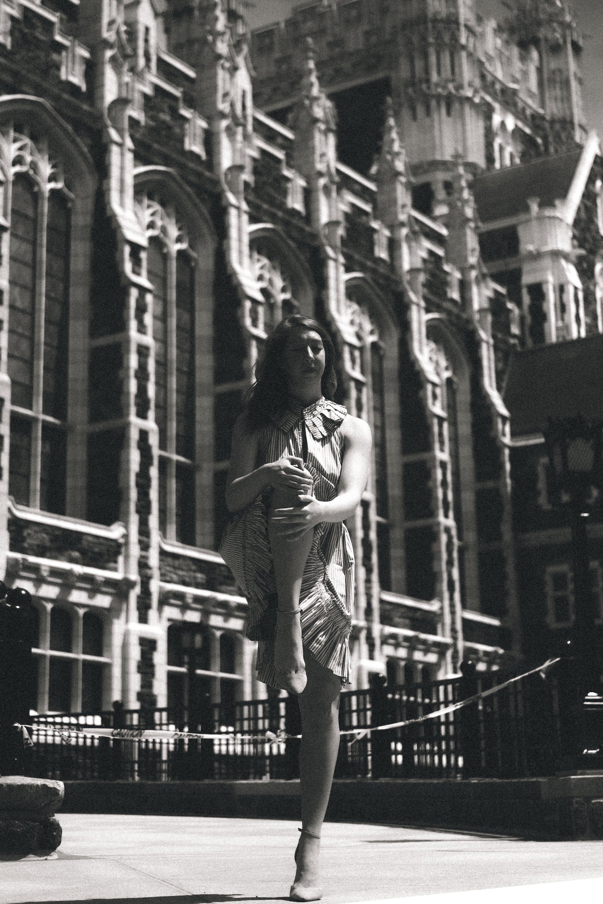 A woman in a striped dress posing on a city sidewalk in front of an ornate, historic building with detailed architectural features.
