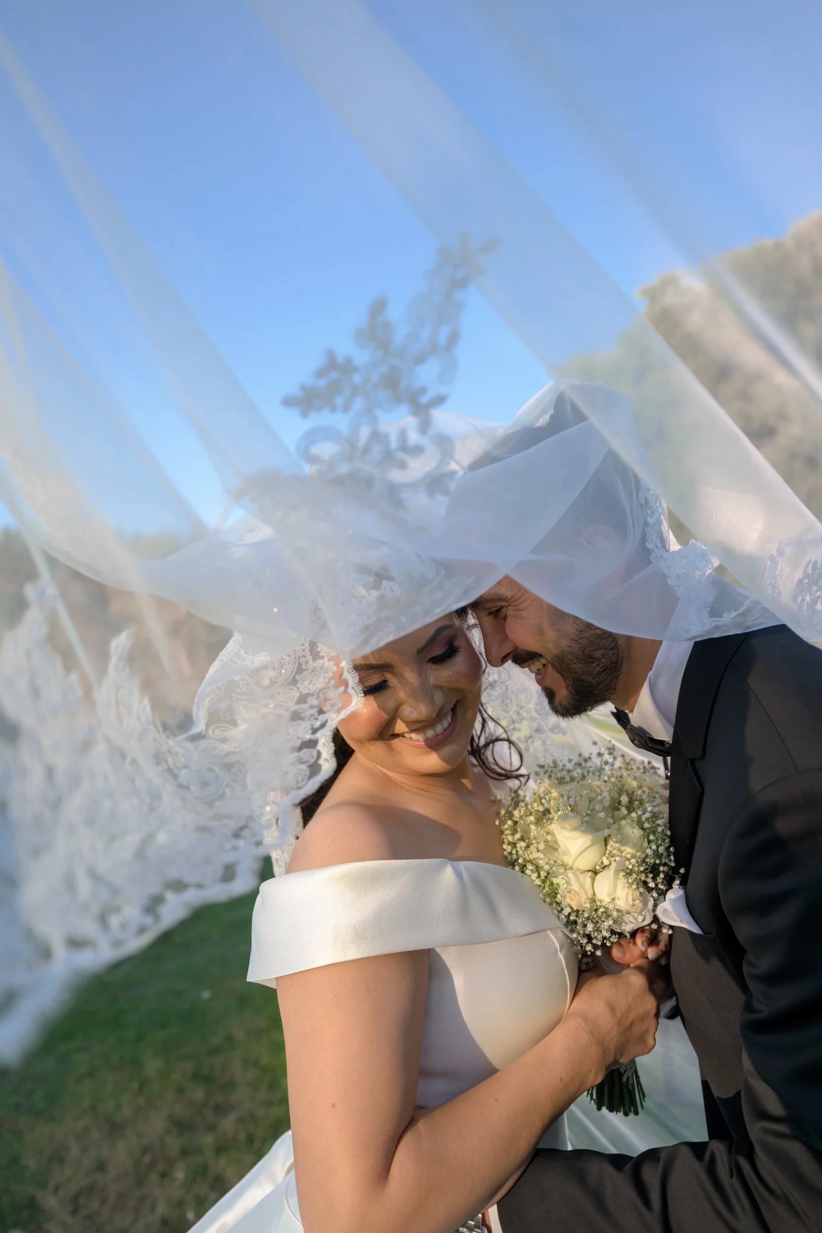 A bride and groom under a veiled canopy, smiling and sharing an intimate moment during their wedding outdoors.