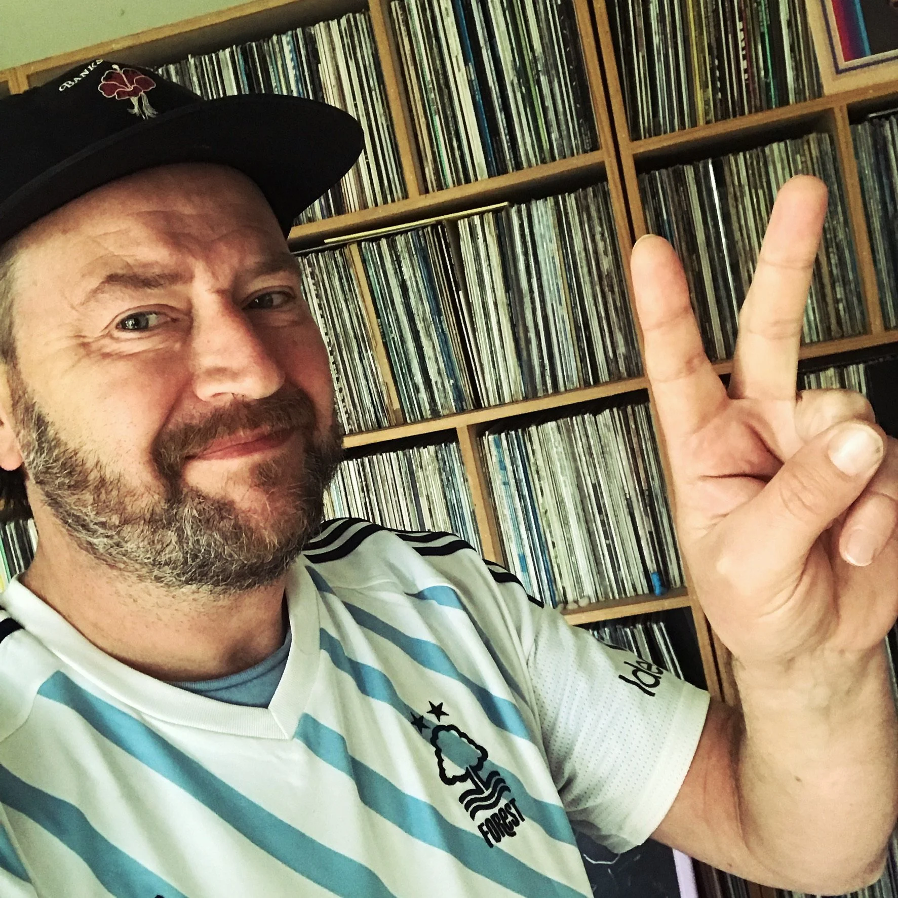 Man against shelf of many records, pulling victory finger sign.