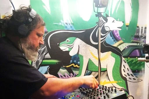 a male DJ playing records agains a bright mural background