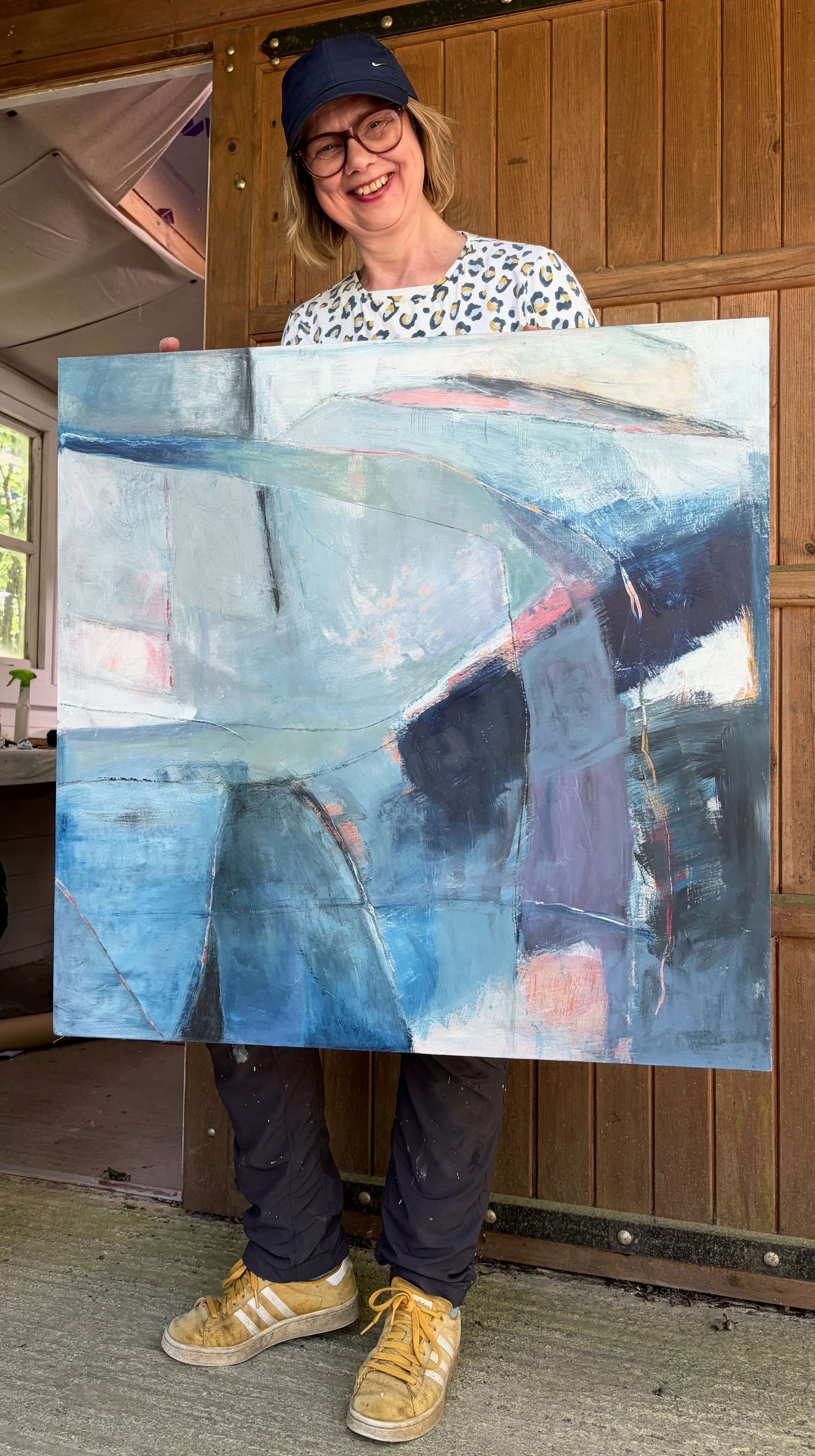 Gera Dunachie standing relaxed in front of her studio holding large blue painting