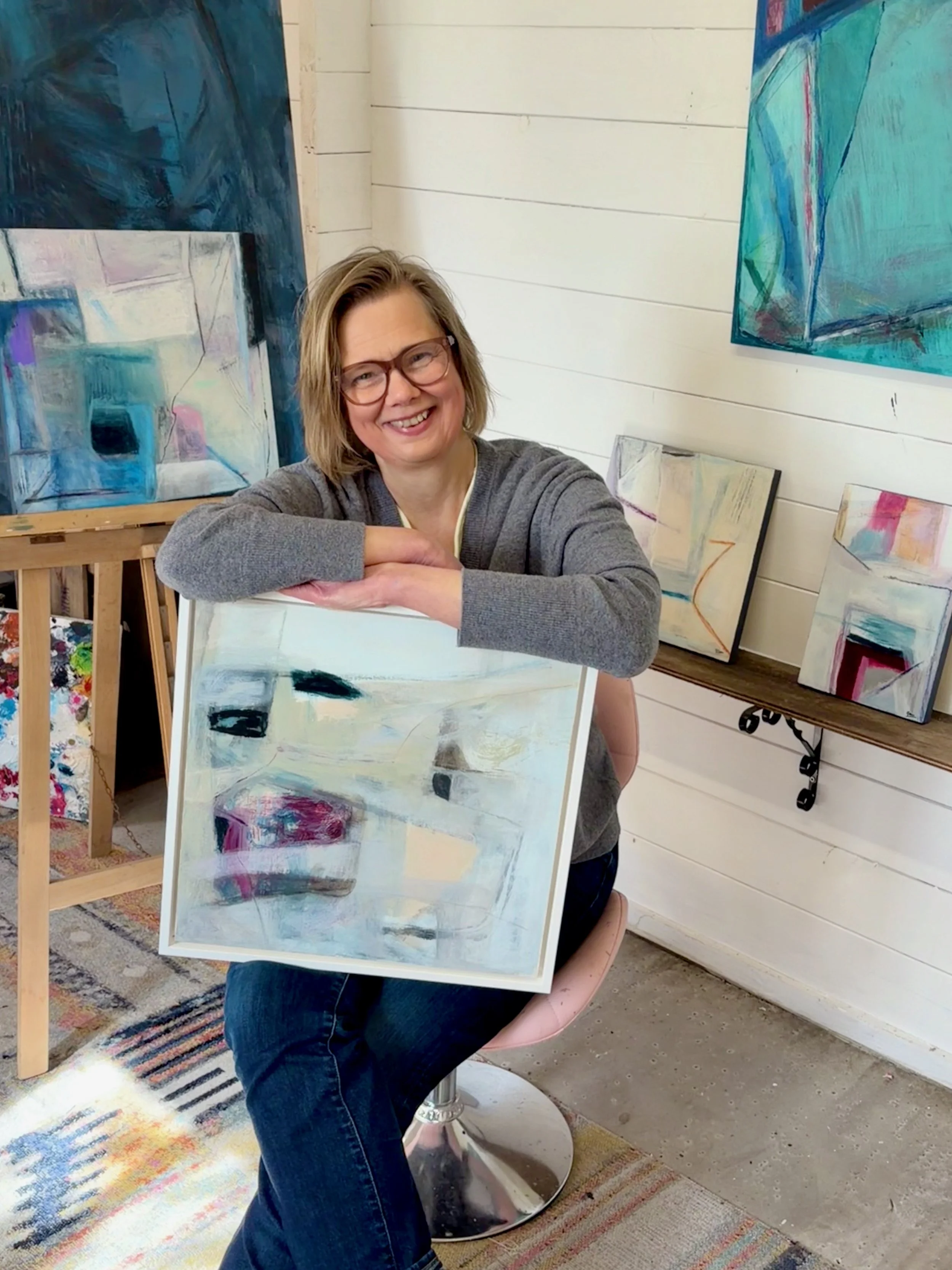 Gera Dunachie sat relaxed in her artist studio holding a painting in a white frame