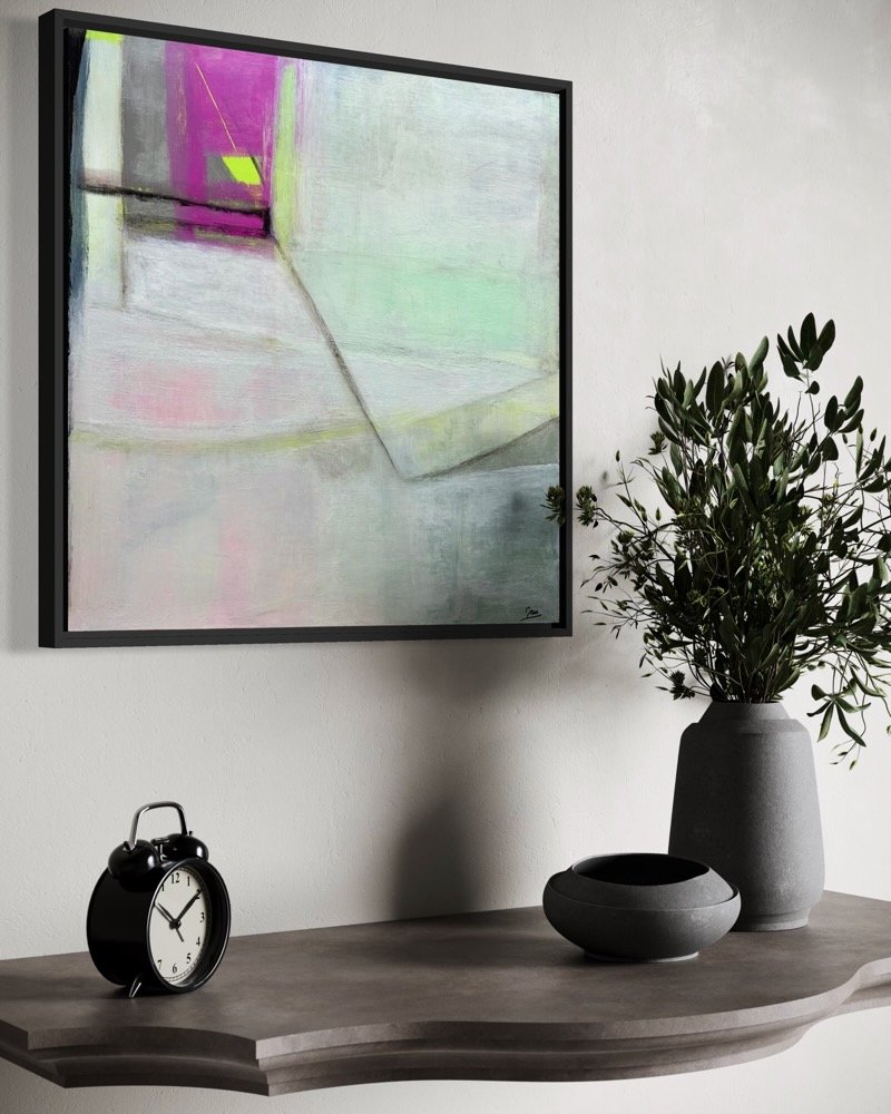 Square framed abstract painting Silent Collision by Gera Dunachie hanging on a white wall above a wooden side table with a black clock, ceramic bowl, and potted plant.