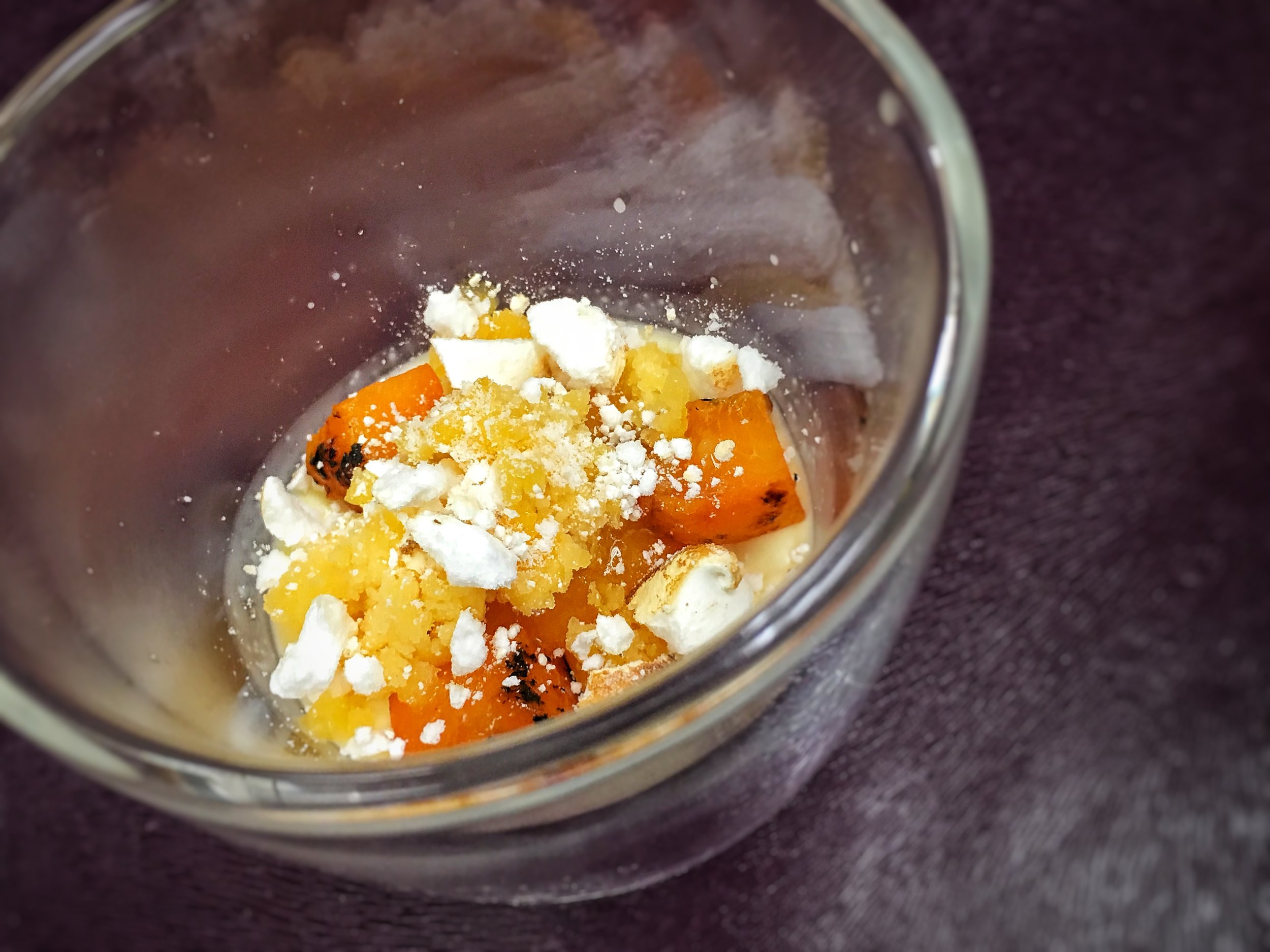 Close-up of a glass container containing broken pieces of roasted sweet potatoes and crumbled white cheese.