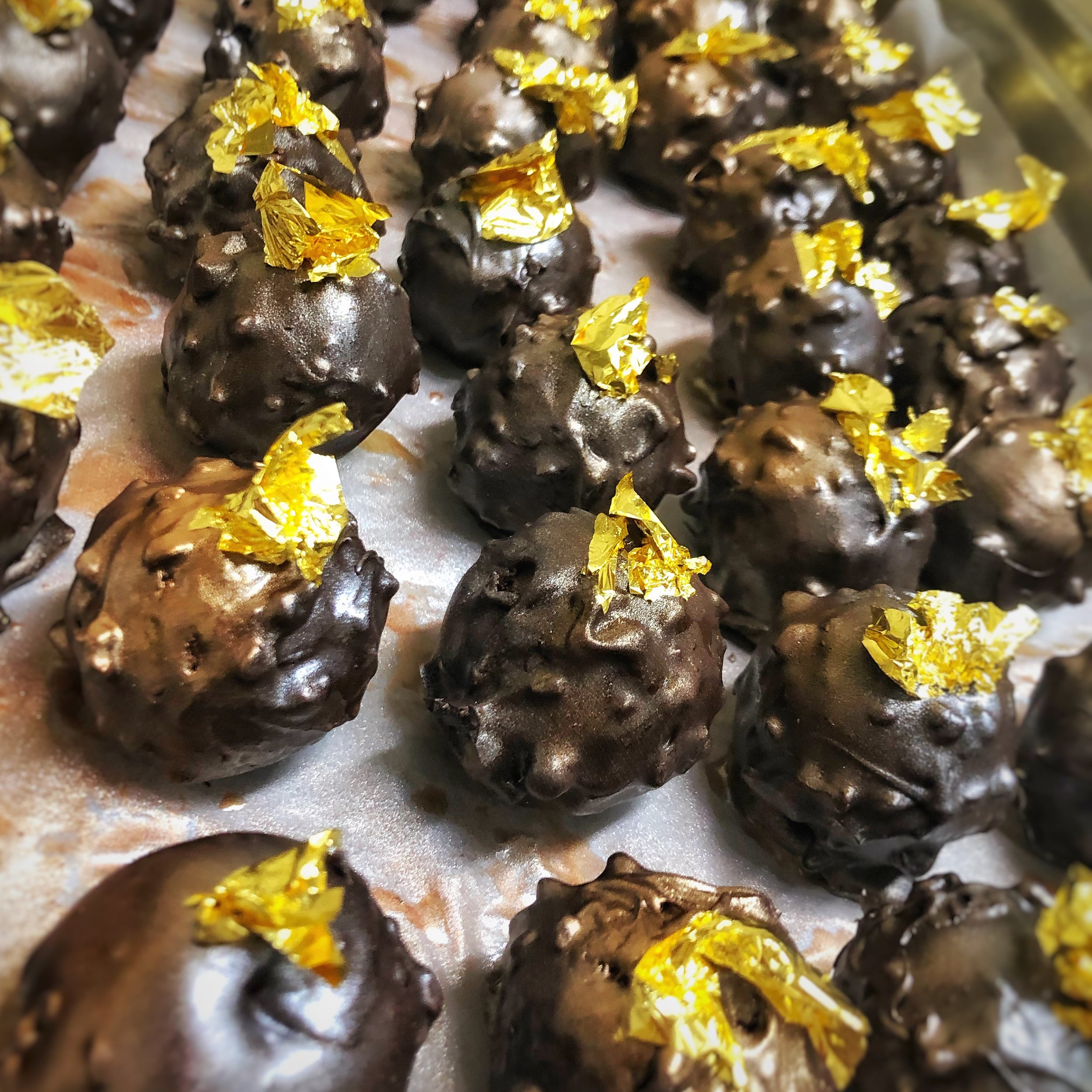 Chocolate truffles topped with gold leaf on parchment paper.