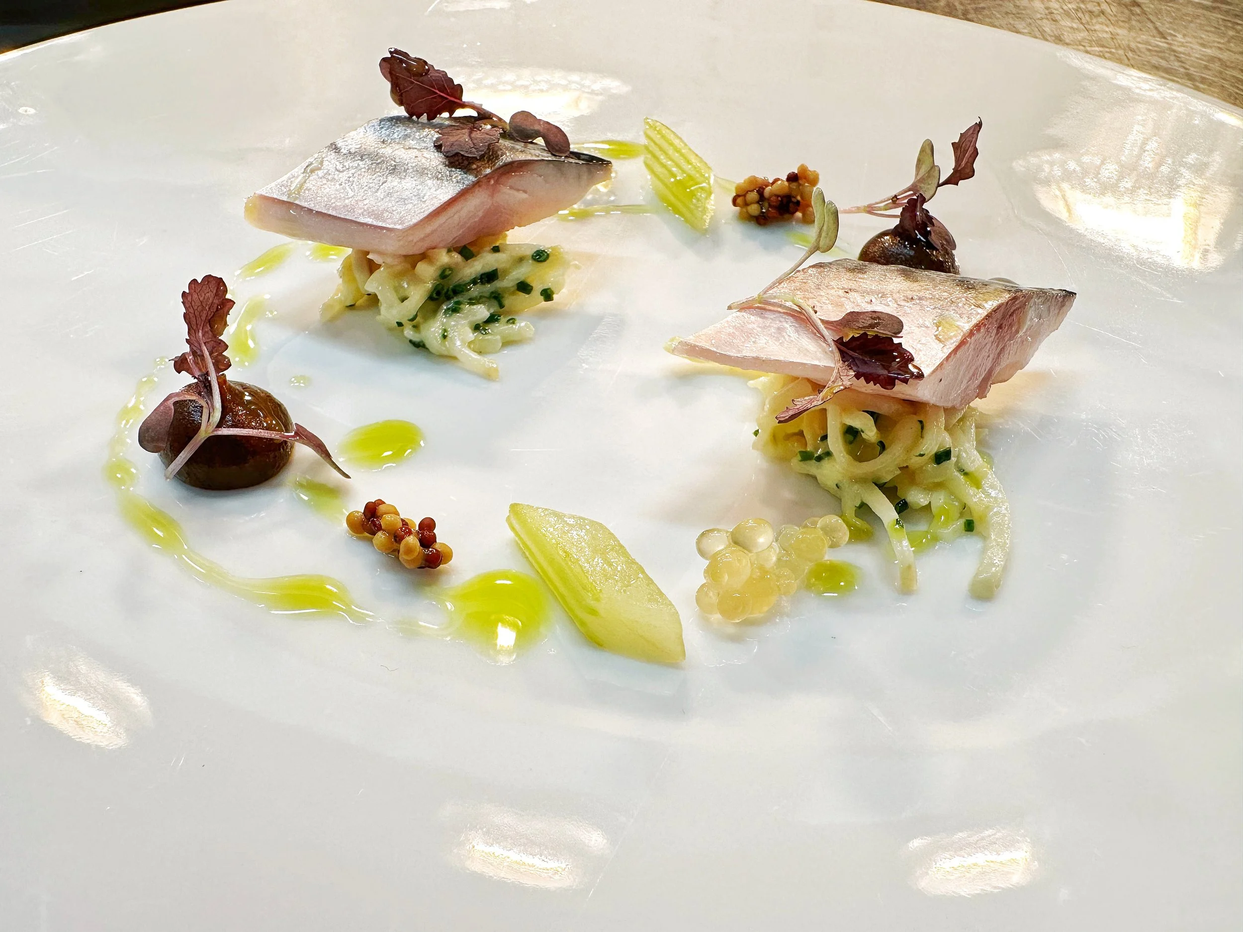 Artistic plated dish with two pieces of seared mackerel on a celeriac remoulade, with baked apple puree and compressed celery