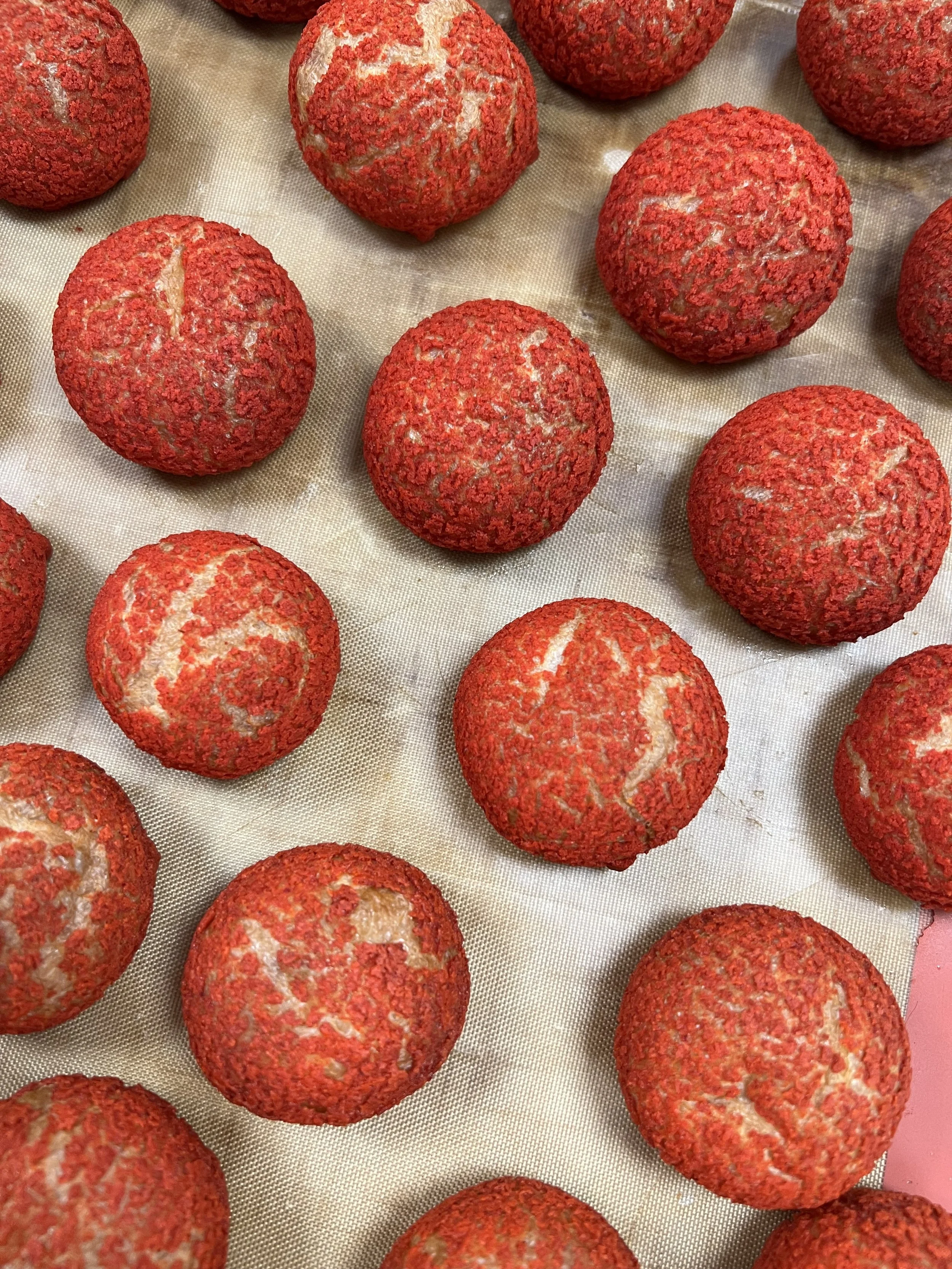 Several bread rolls covered in red poppy seeds on a baking sheet.