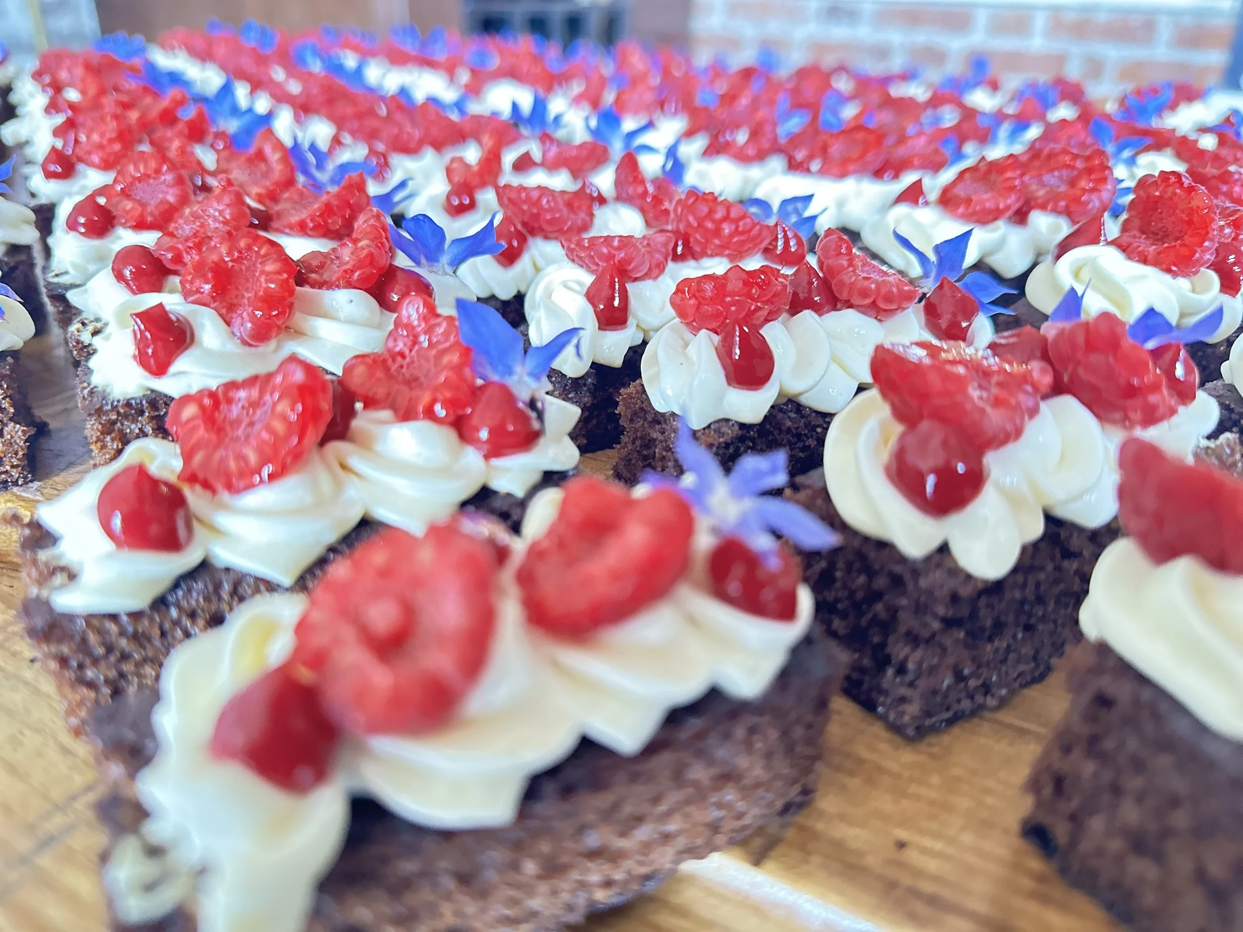 Close-up of chocolate cake slices with white frosting, topped with red raspberries and blue edible flowers.