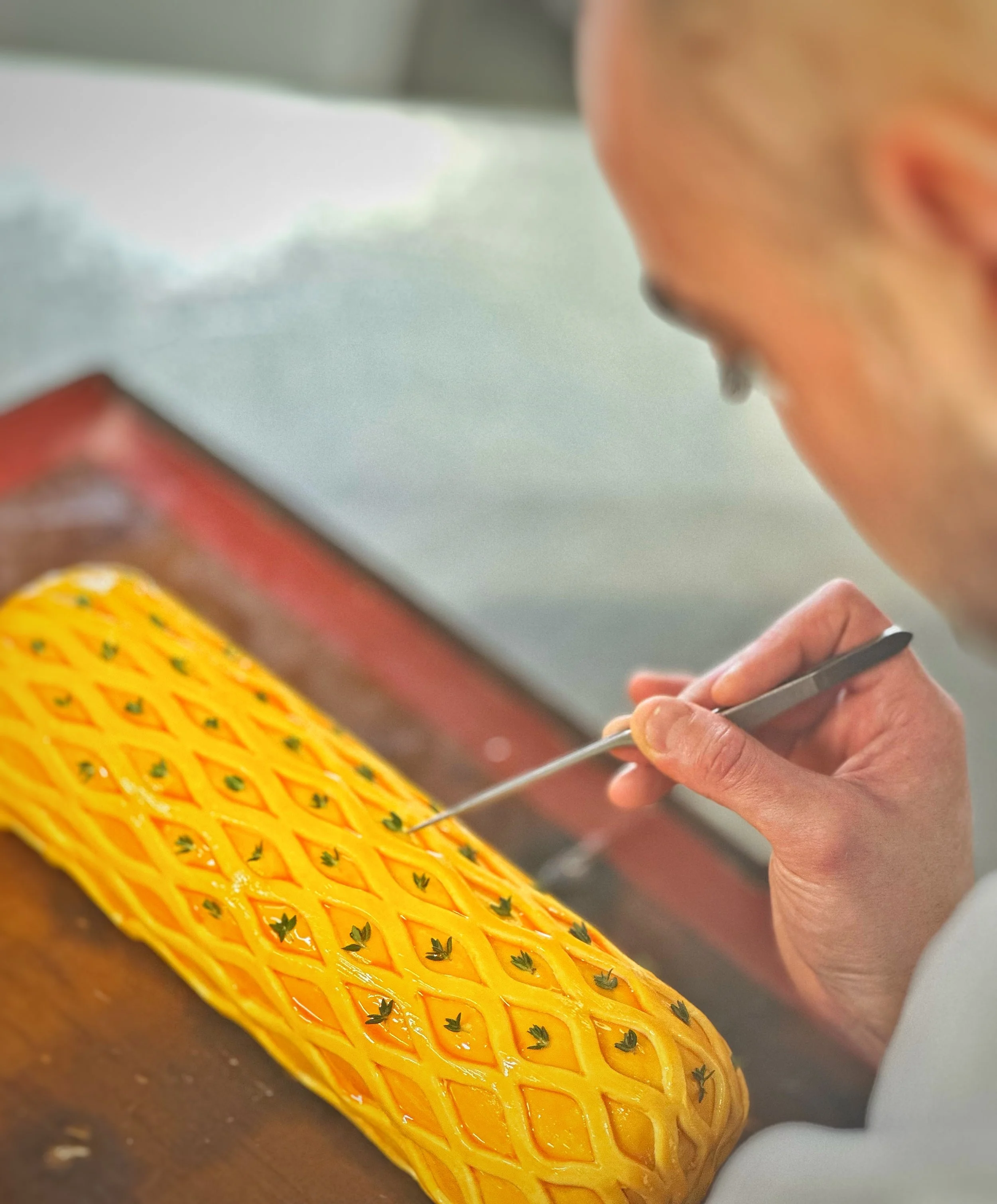 Chef Carl Cleghorn decorating a beef wellington with a small tool, in a professional kitchen.