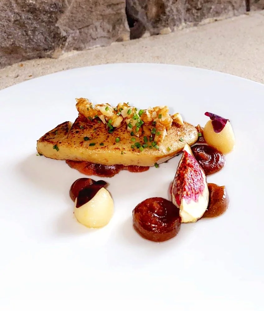 Pan-seared fish fillet garnished with chopped herbs and a topping of crispy onions, served with dollops of creamy mashed potatoes, and small fruit or vegetable accompaniments on a white plate.