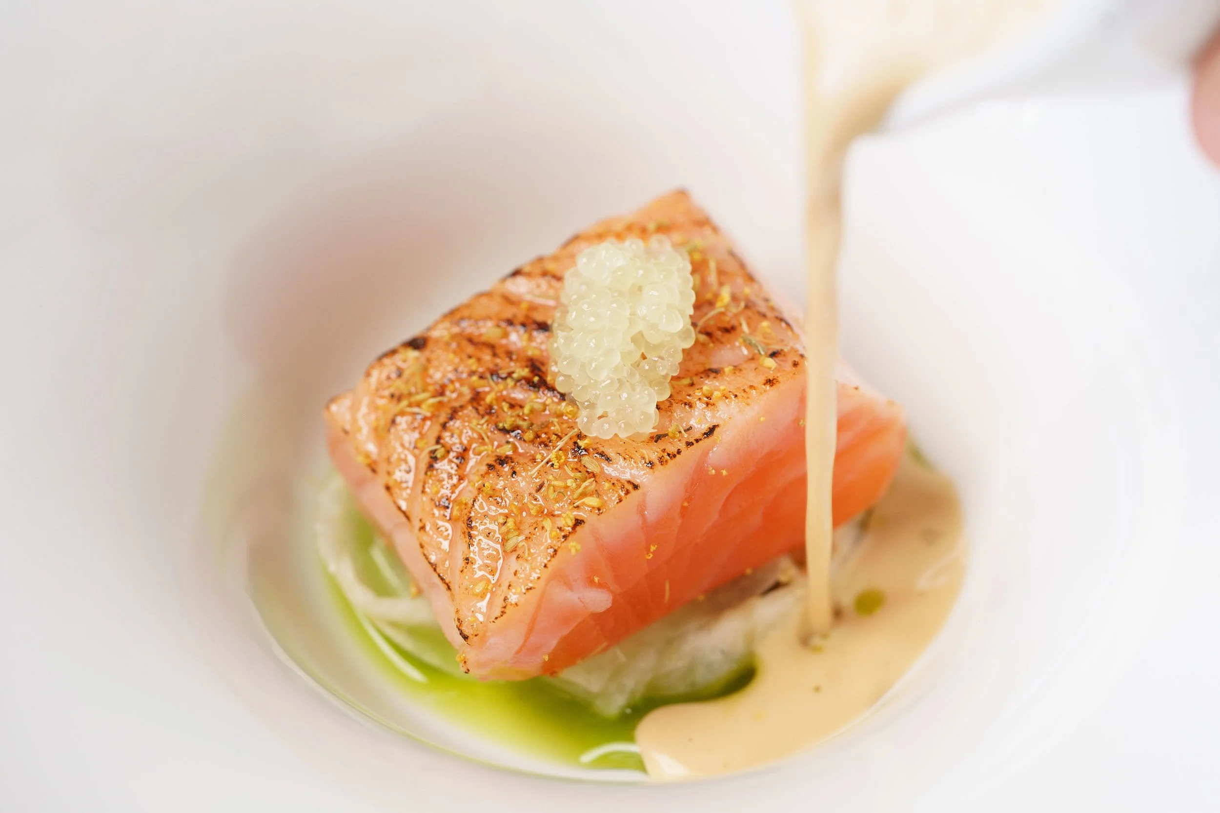 Pan-seared salmon filet topped with caviar, served with a light sauce and garnished with herbs.