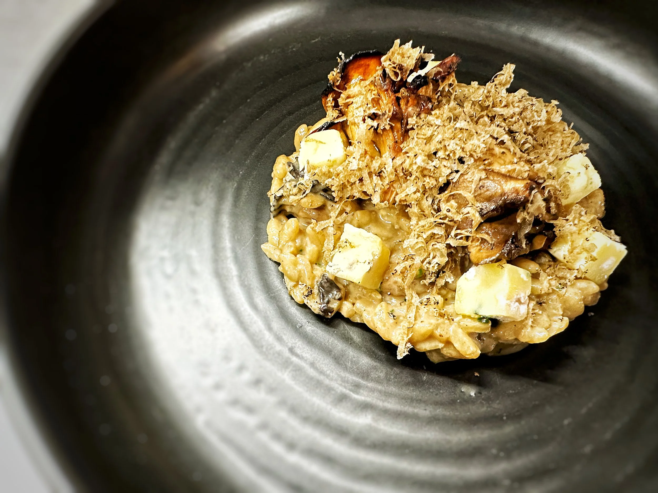 A serving of risotto with mushrooms, cheese, and fresh grated black truffle in a black bowl.