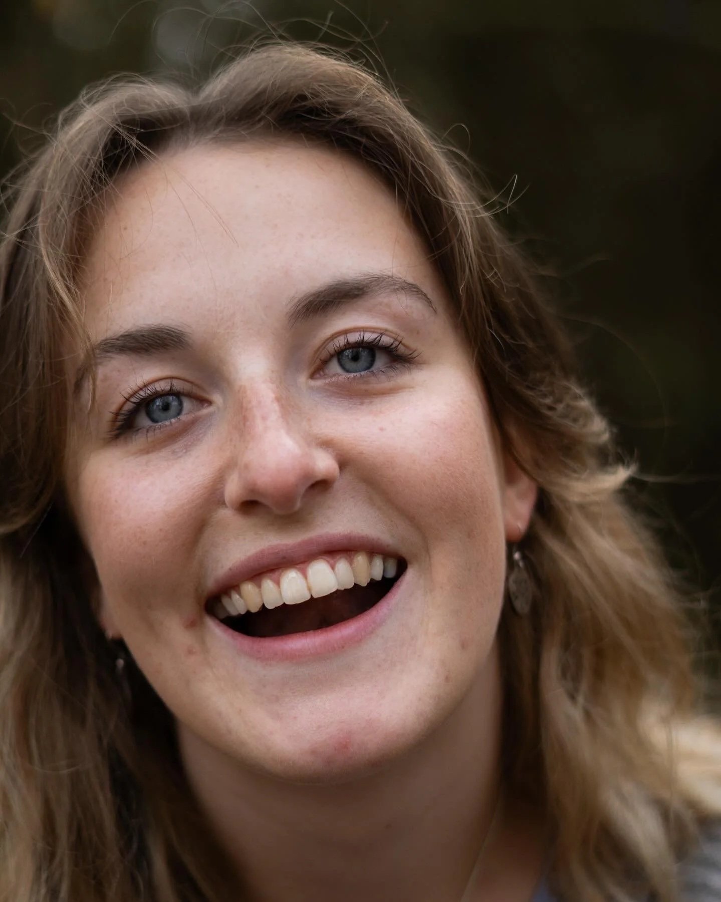 Close-up of a smiling woman with blue eyes and light brown wavy hair.