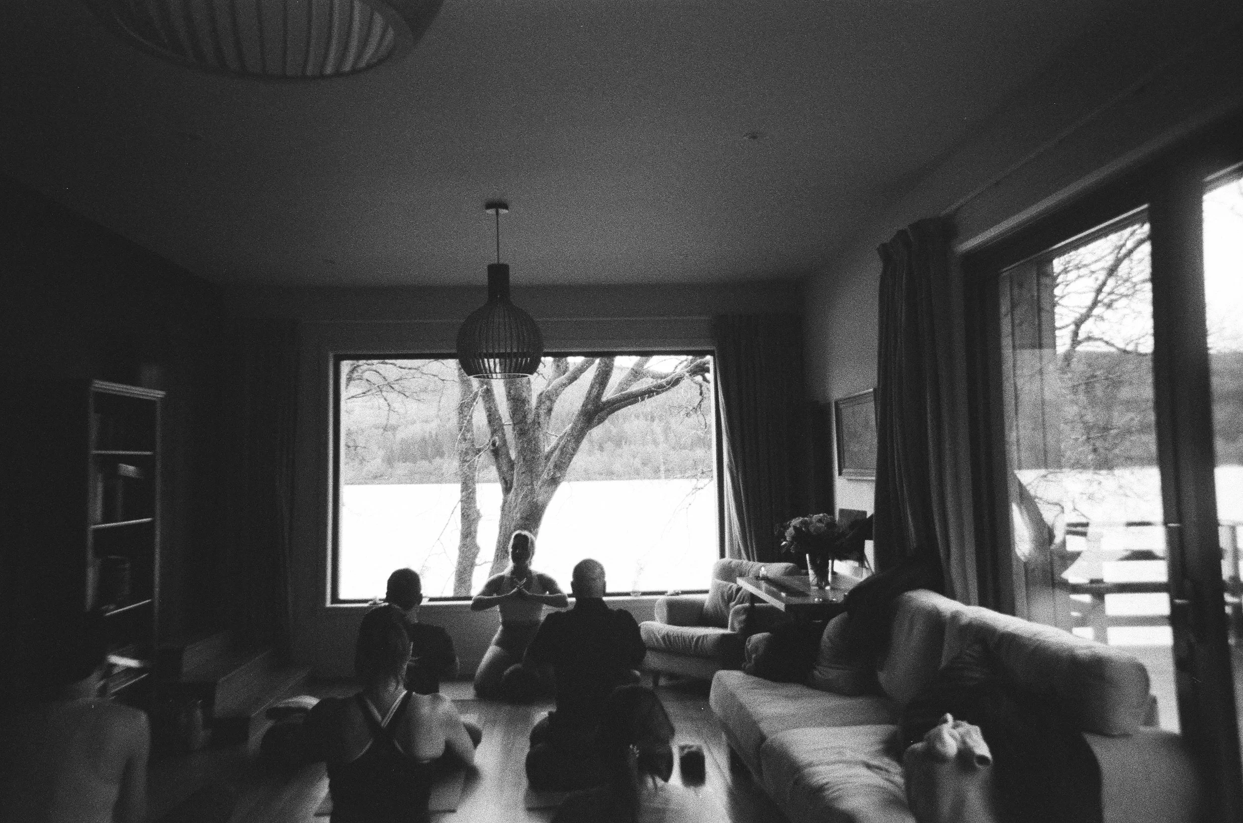 People practicing yoga in a living room with large windows and a view of a snowy landscape.