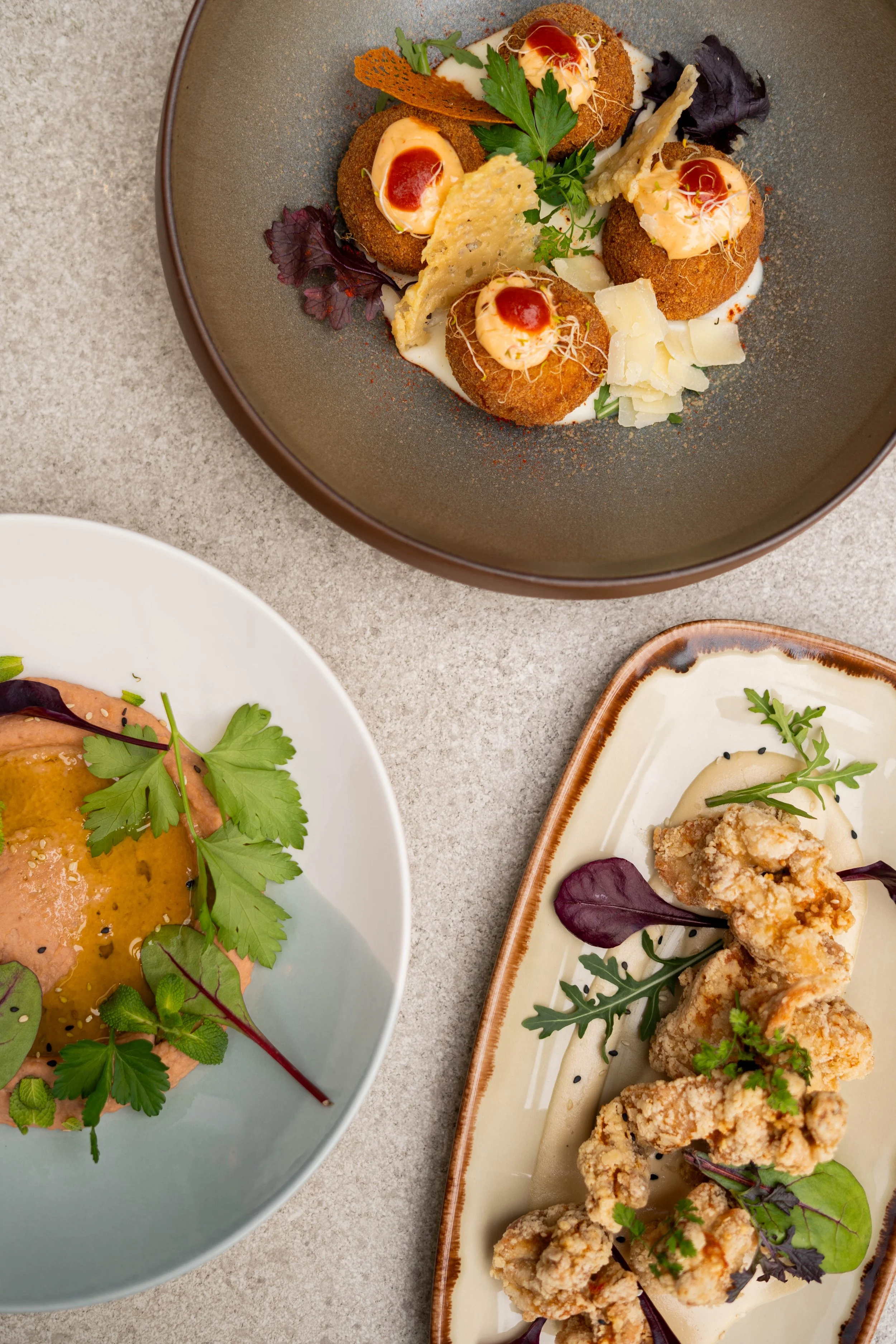 Assortiment de plats avec des boulettes croustillantes, une tartine avec une sauce rose, et des morceaux de poulet frit, garnis de feuilles de salade et herbes.