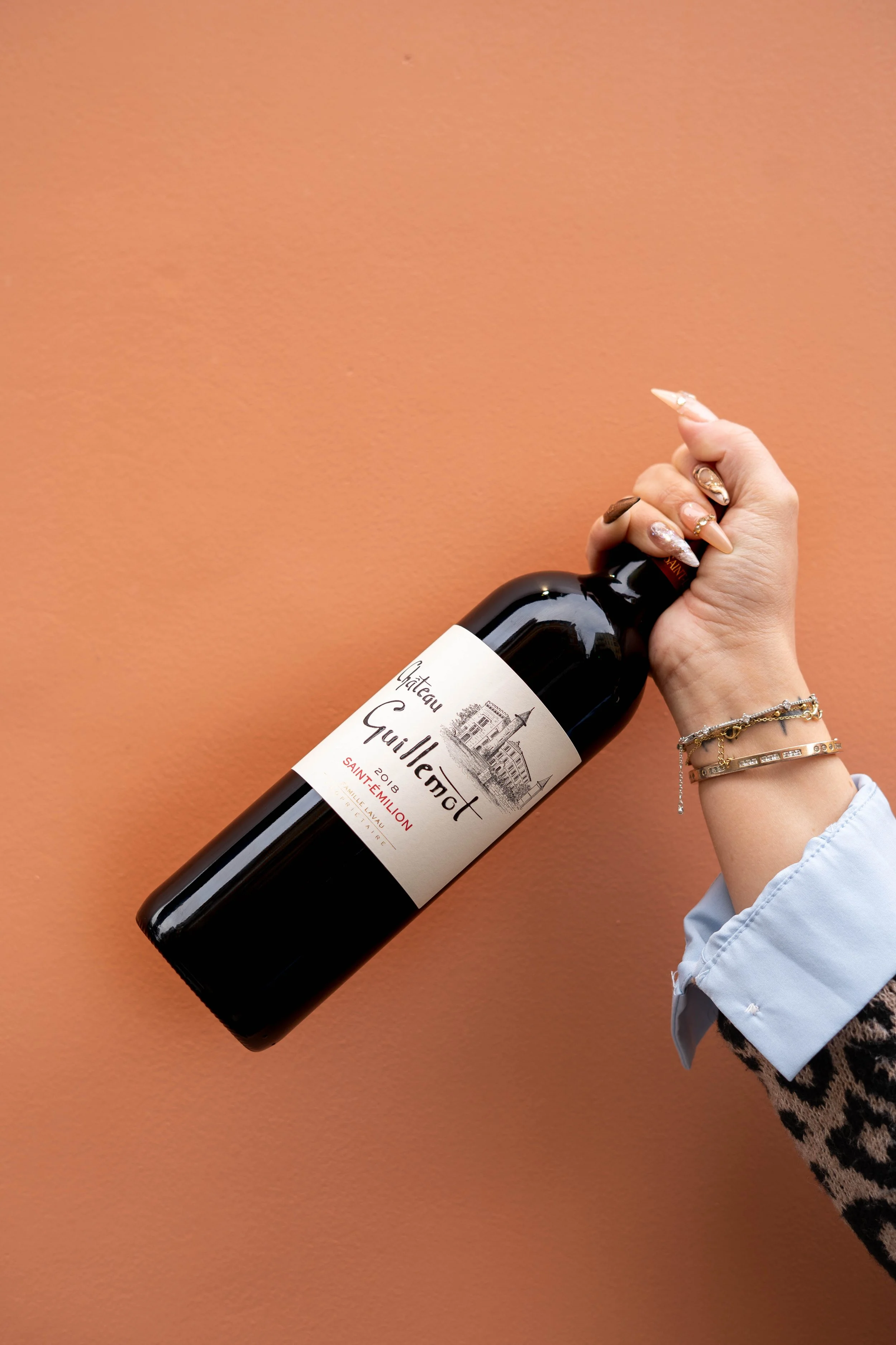 Une main tenant une bouteille de vin rouge contre un mur orange