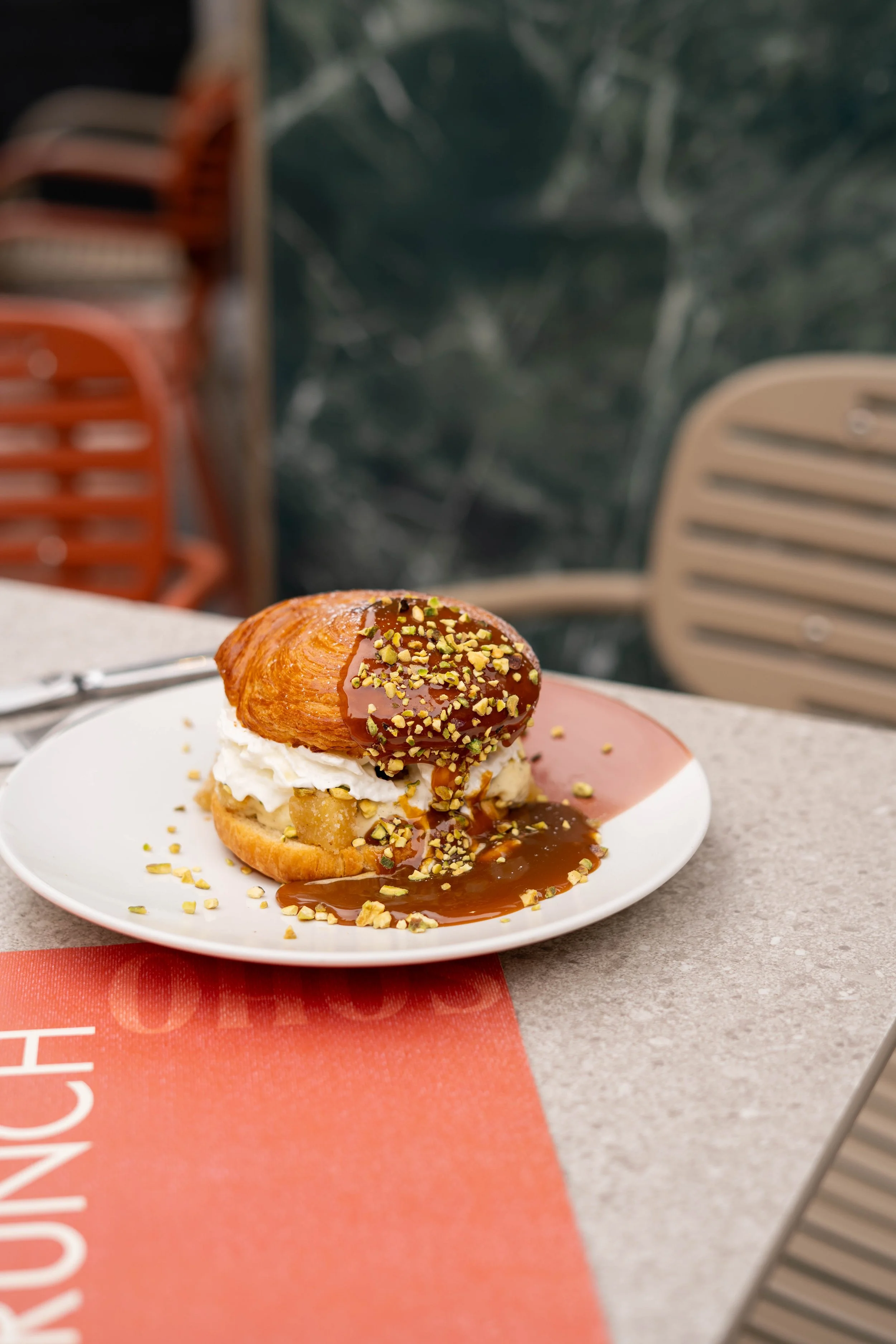 Un dessert avec une pâtisserie à la crème, garnie de caramel, de noix hachées, avec une base de pâte, sur une assiette blanche.