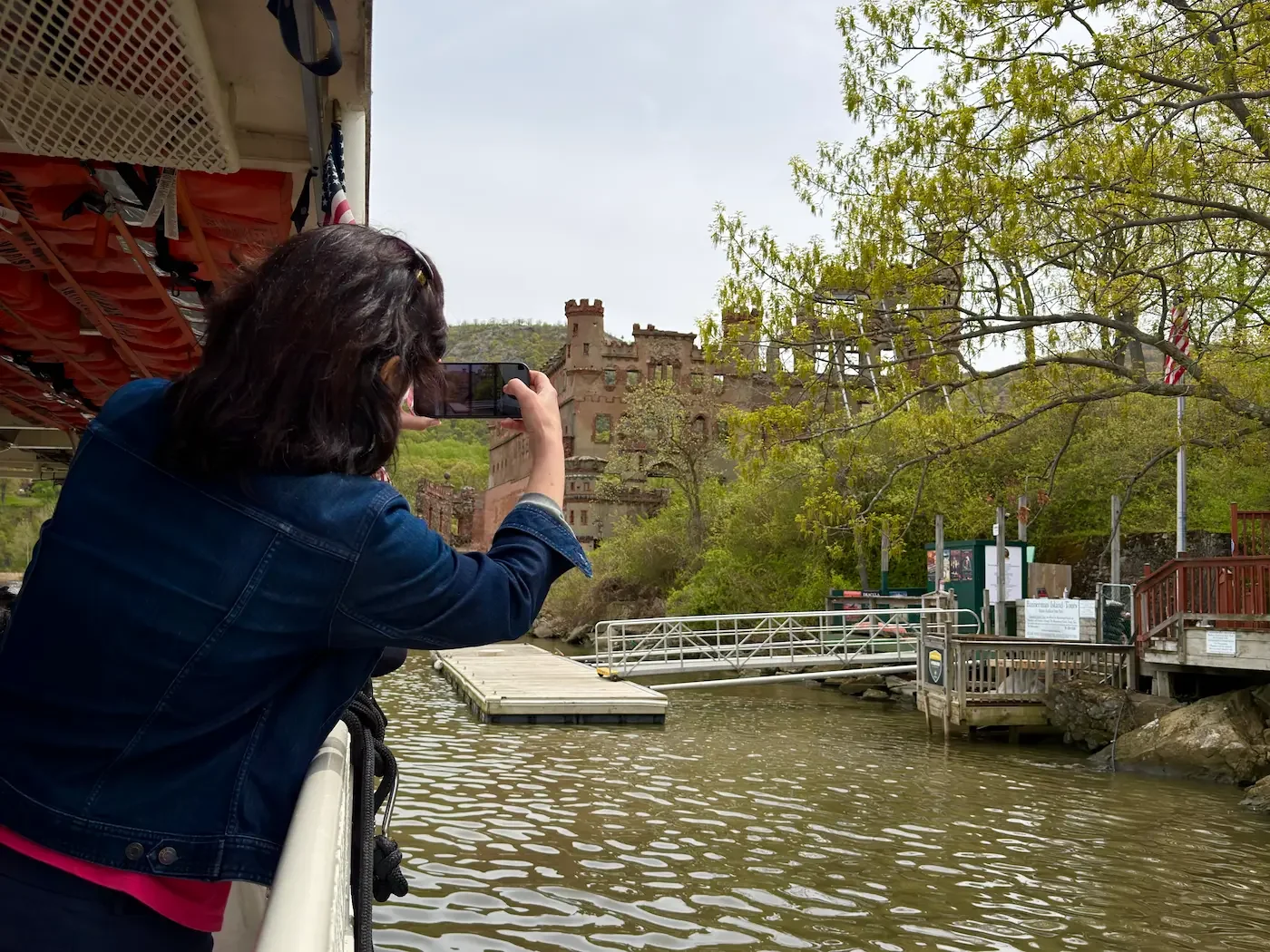 A tourist takes a photo of Bannerman Castle and island with an iphone from a boat on the river