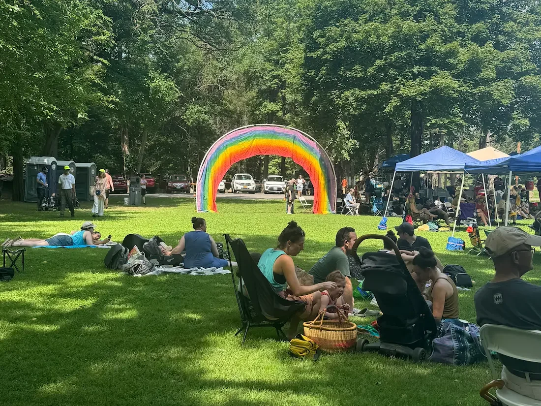 people picnic sitting on the ground with rainbow arch in background