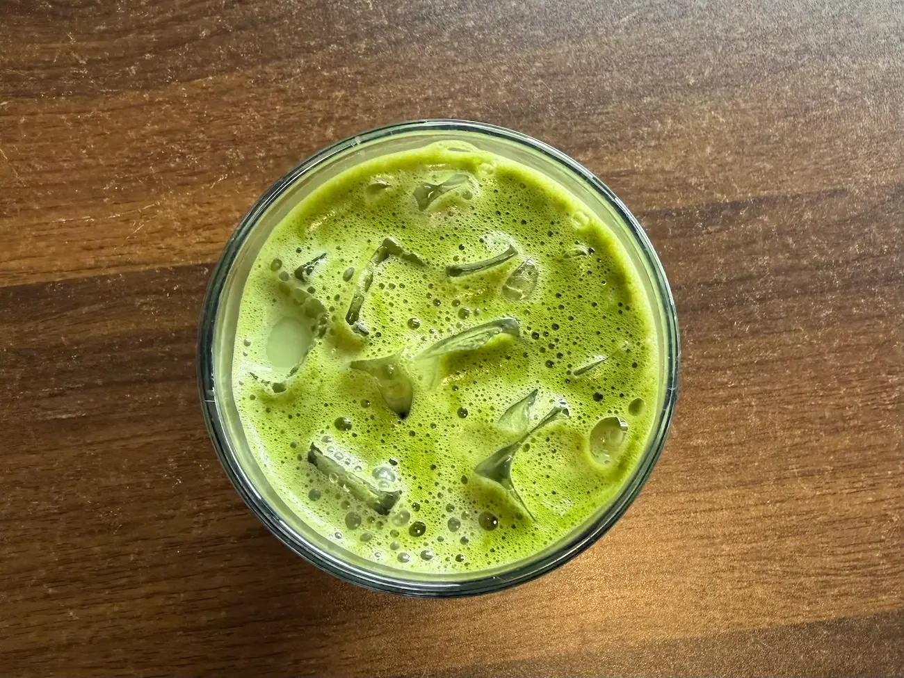 an aerial view of a glass of iced matcha latte sits on a wooden table.
