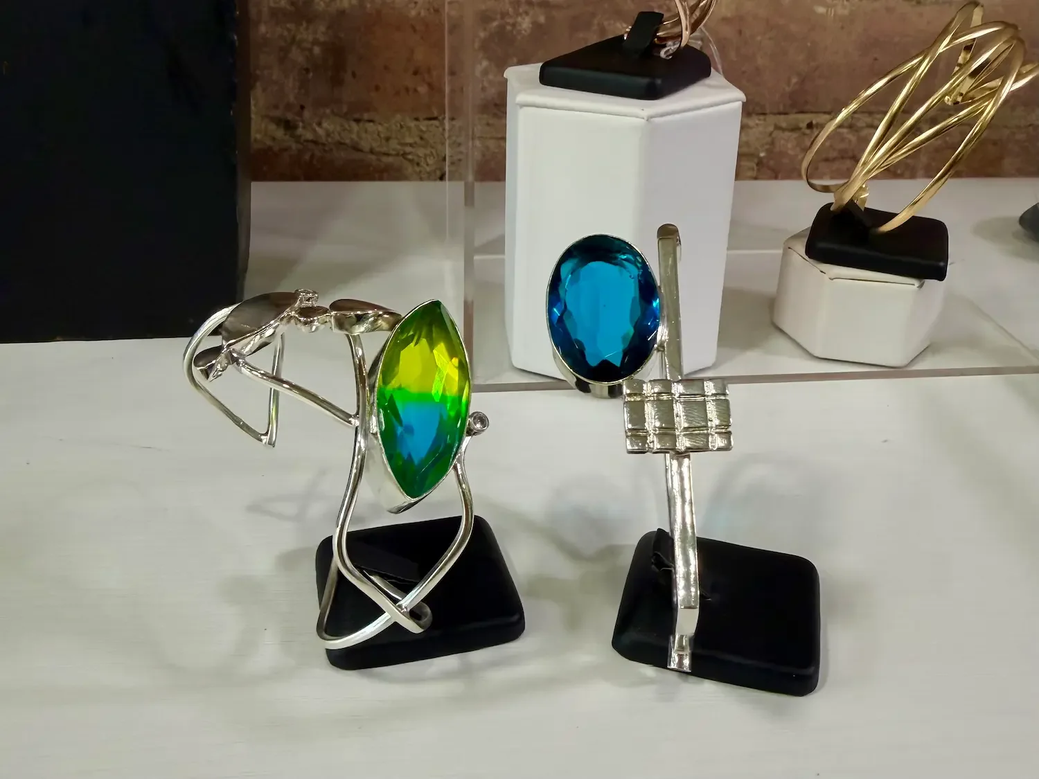 Two silver bracelets, one with a green gemstone, the other with a blue gemstone sitting in a jewelry store