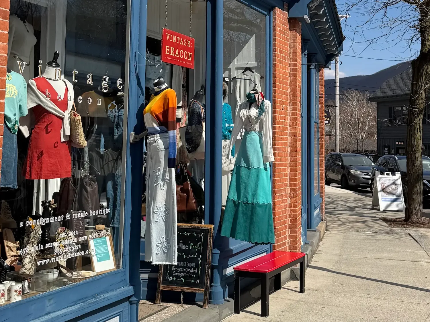 A vintage store with colorful clothes hanging outside on a sunny day.