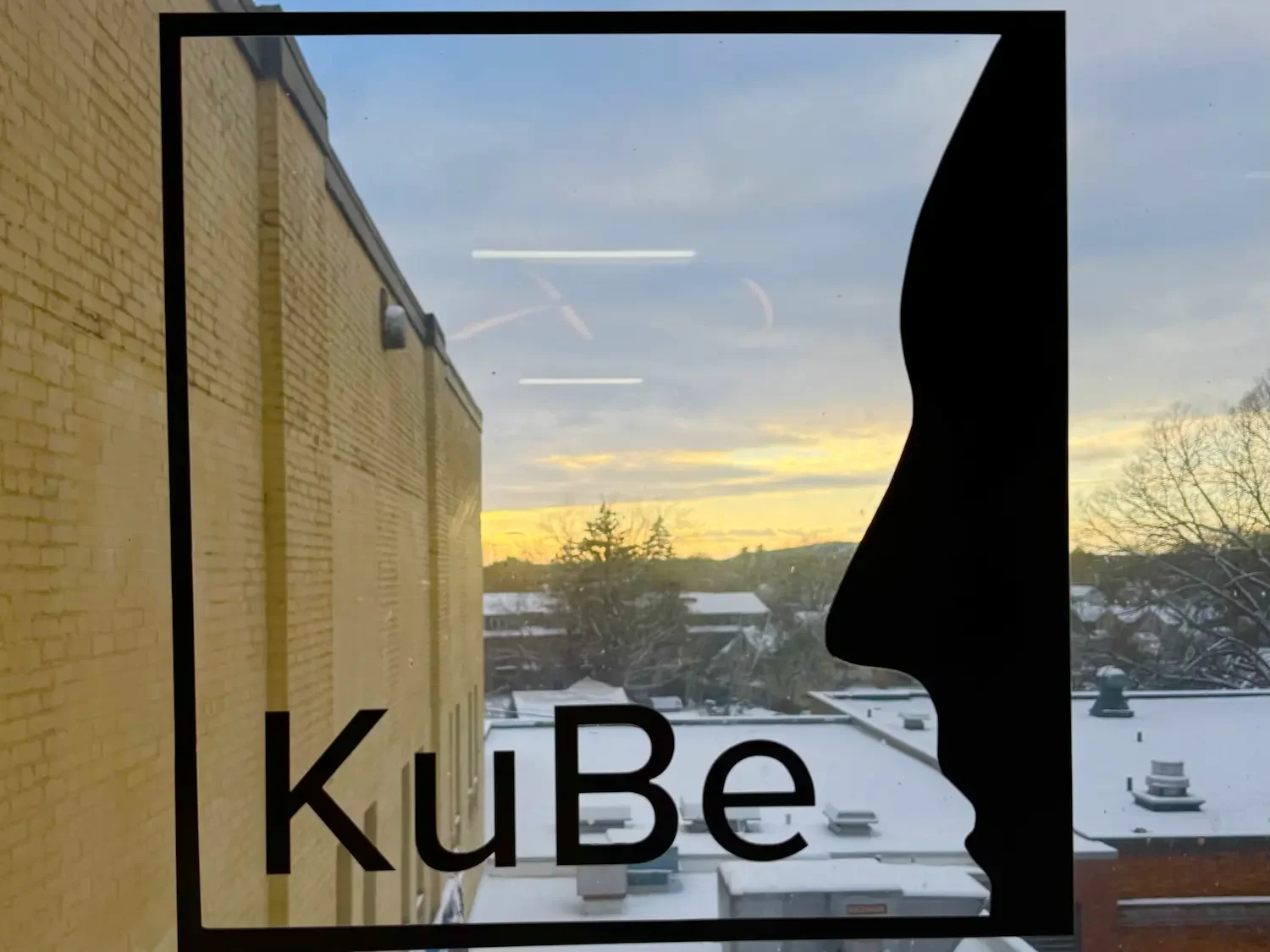 A decal of KuBe art center's logo on a window with a sunset in the background