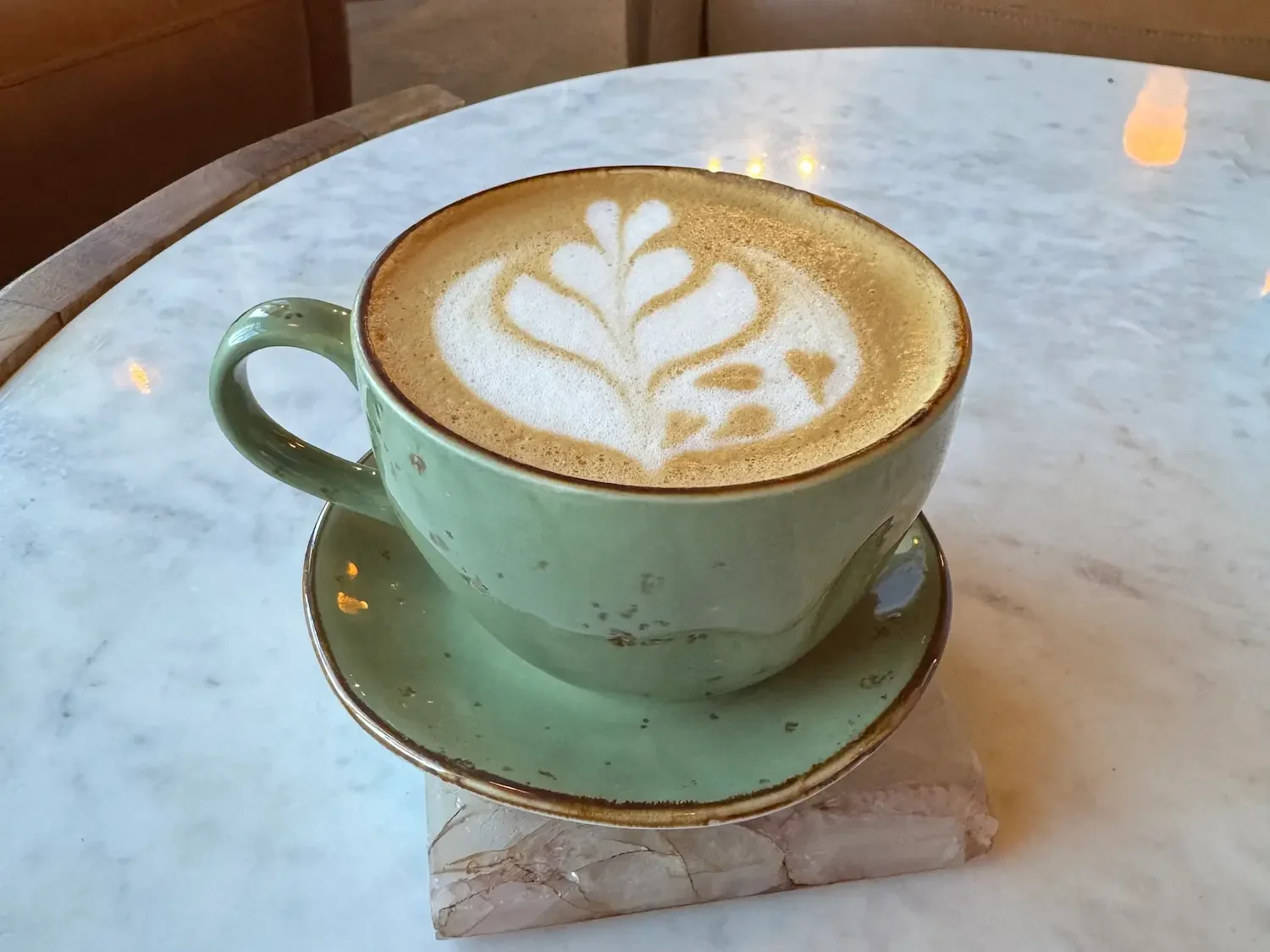 capuccino coffee in green cup and saucer on marble table