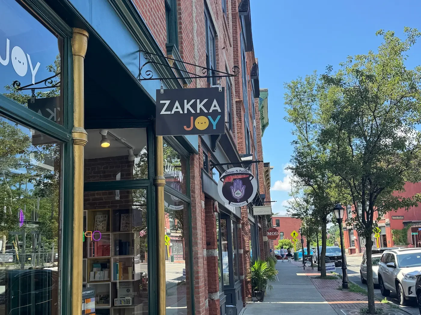 A line of shopfronts on a tree-lined street with people walking in the background