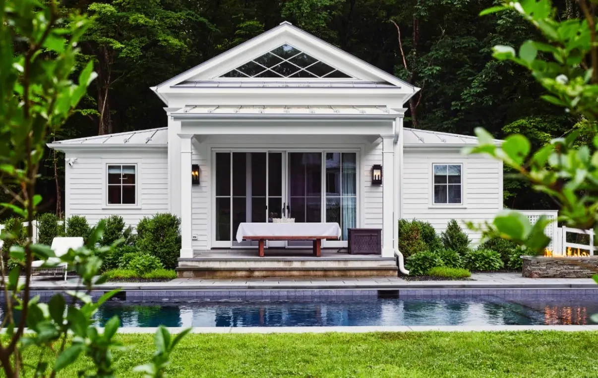 a white building with windows sits behind a swimming pool in a garden