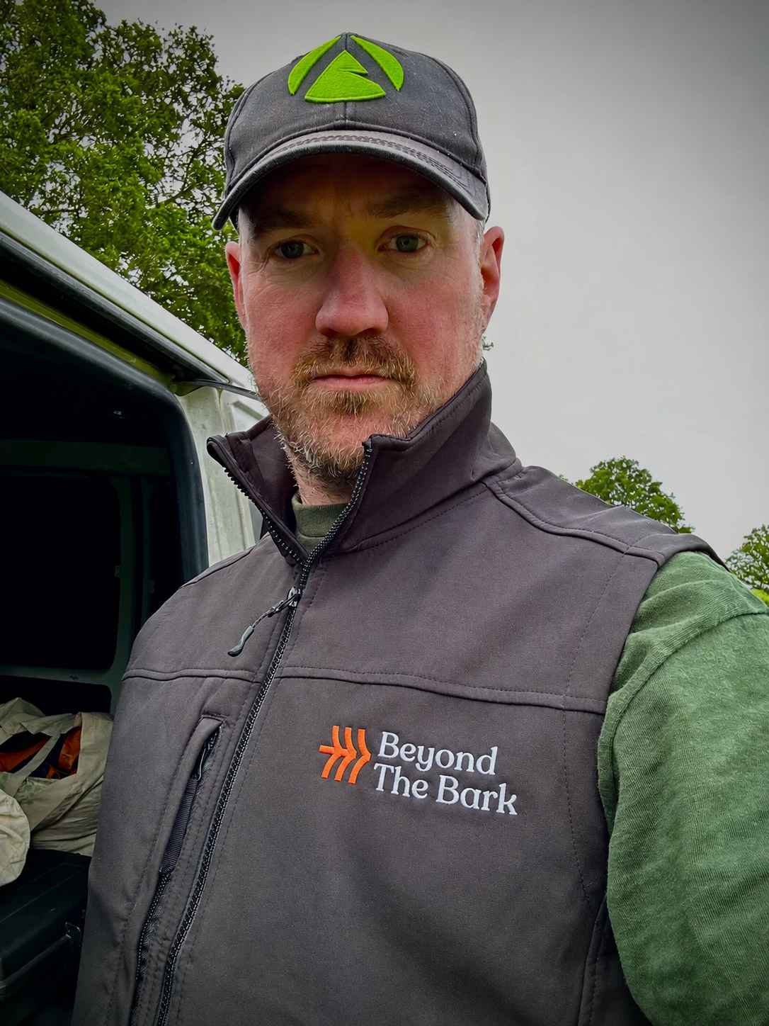 Owner, Phil Johnson stood with trees in the background wearing  a black cap and grey Beyond the Bark branded gilet.