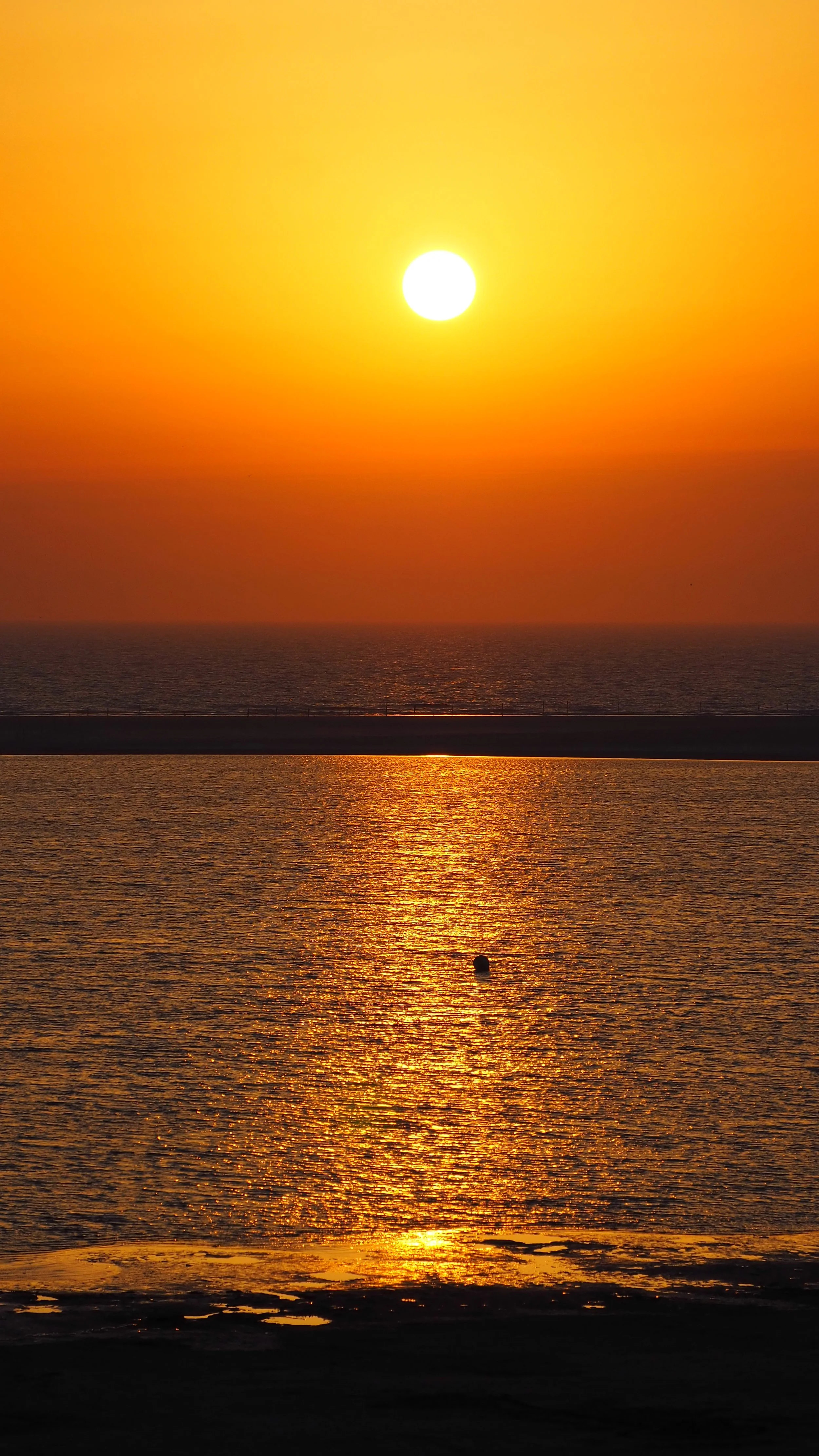 Sonnenuntergang über dem Meer mit reflektierendem Wasser, Horizont und einem einzelnen Boot im Wasser.