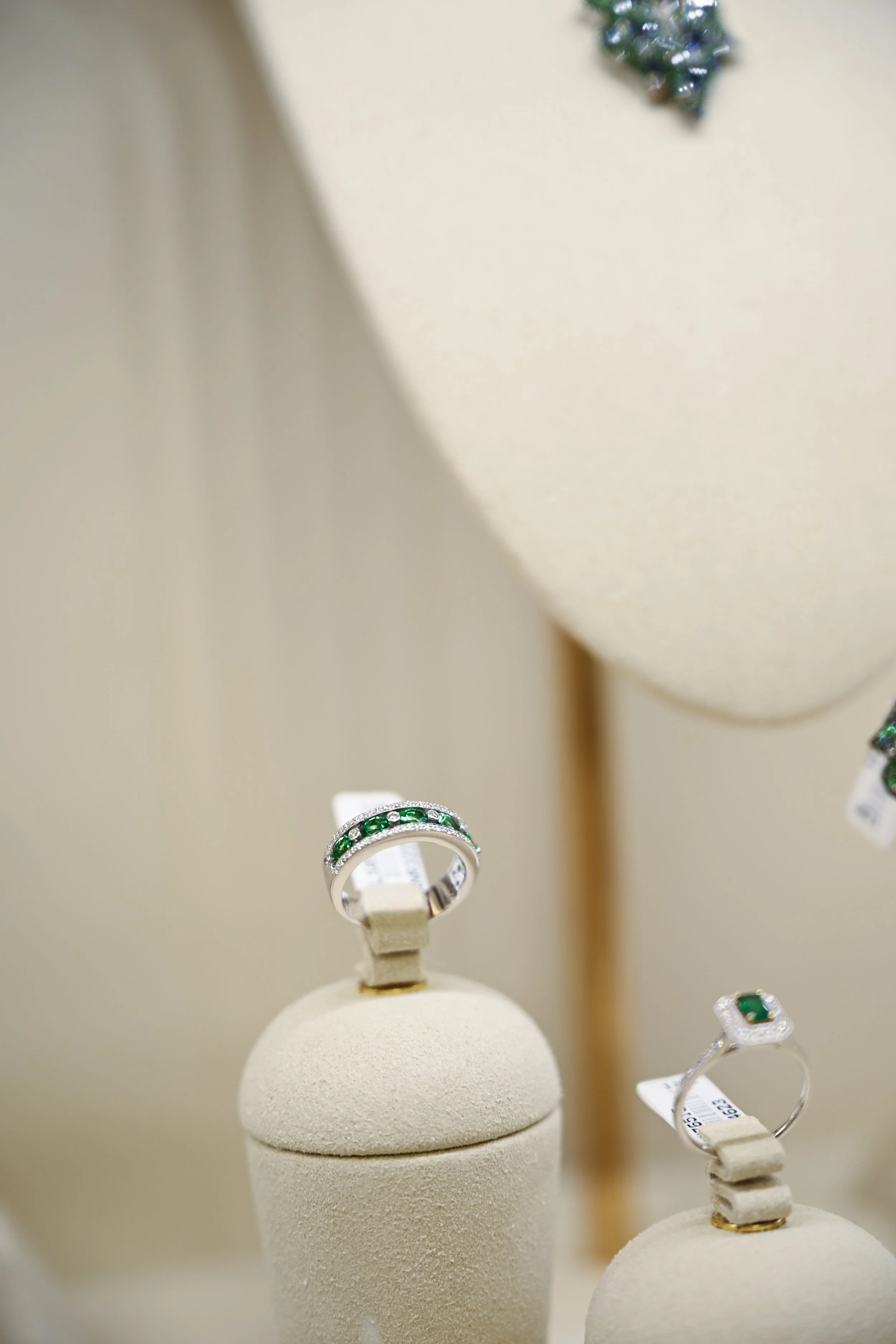 Jewelry display showcasing a silver ring with green gemstones and a matching ring with a green gemstone and diamond accents in a jewelry store.